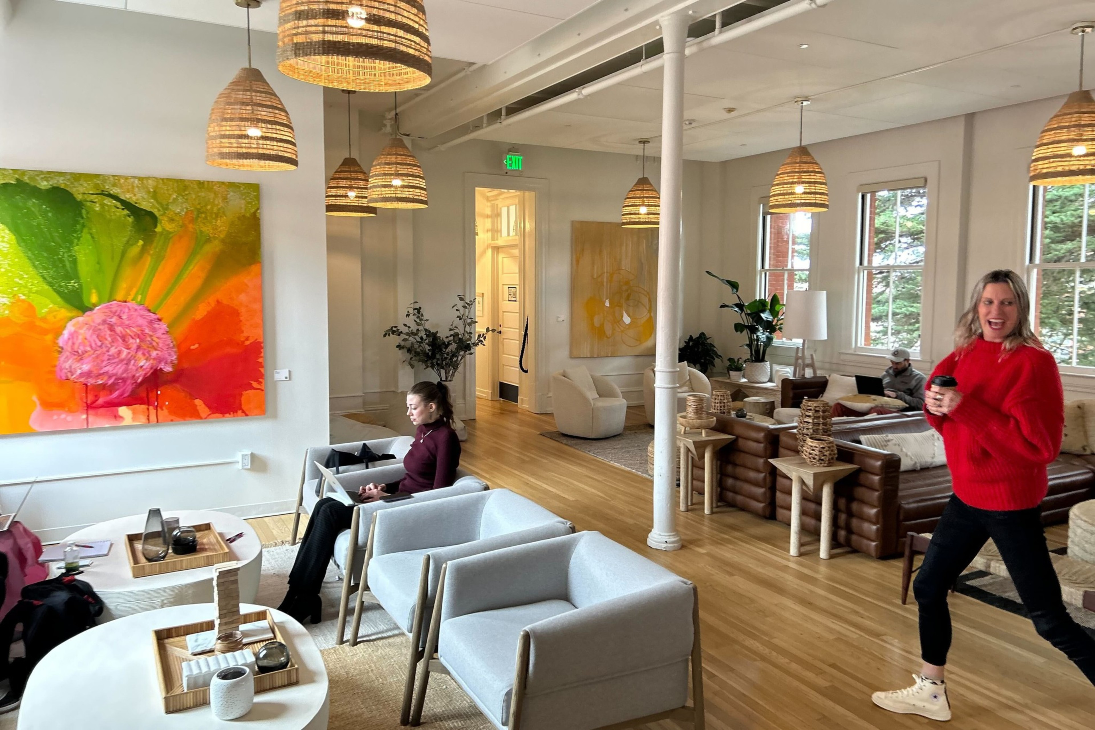A bright modern lounge with people, colorful art, wicker lighting, and comfy seating.