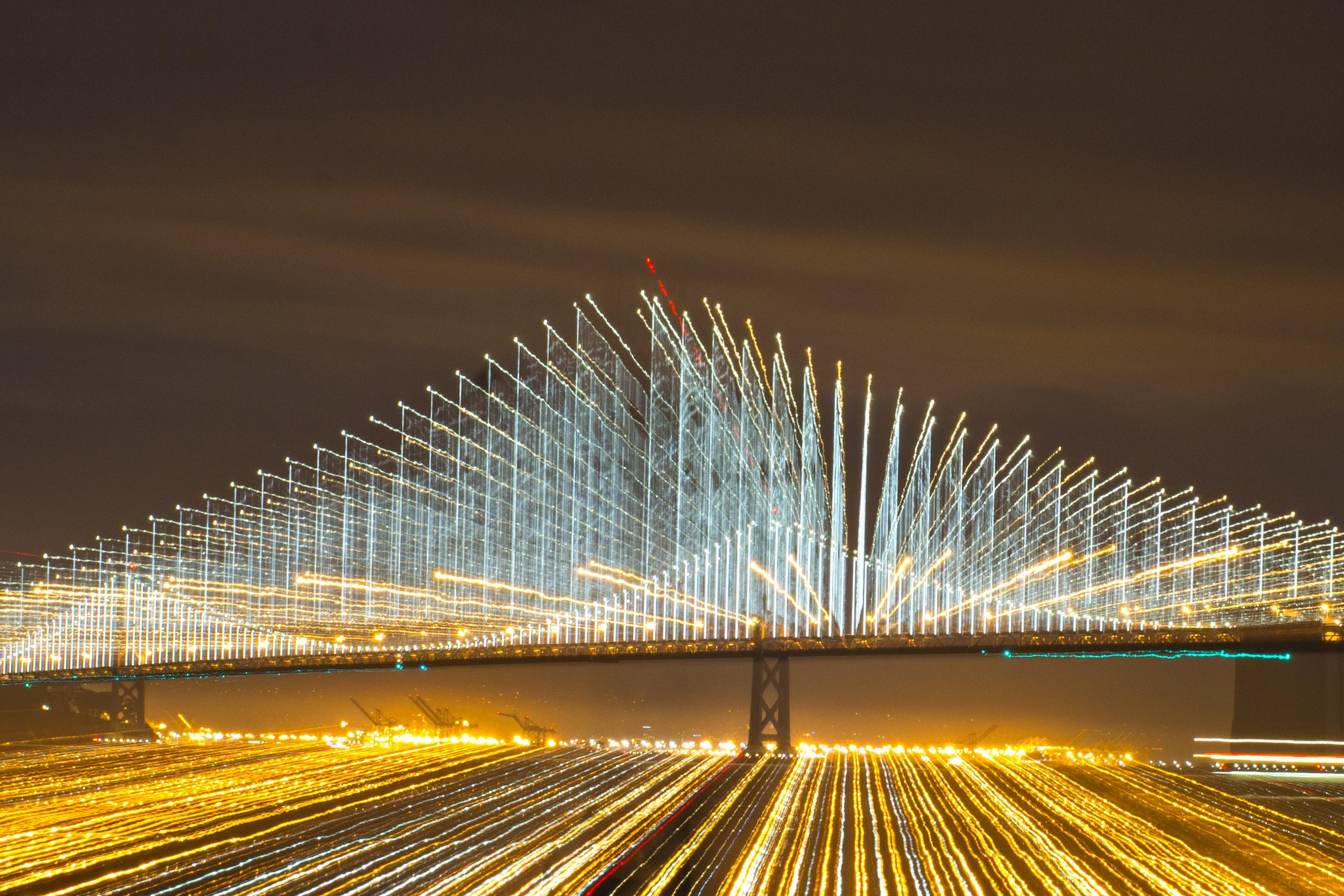 A light show illuminating cables on a suspension bridge shine at night.