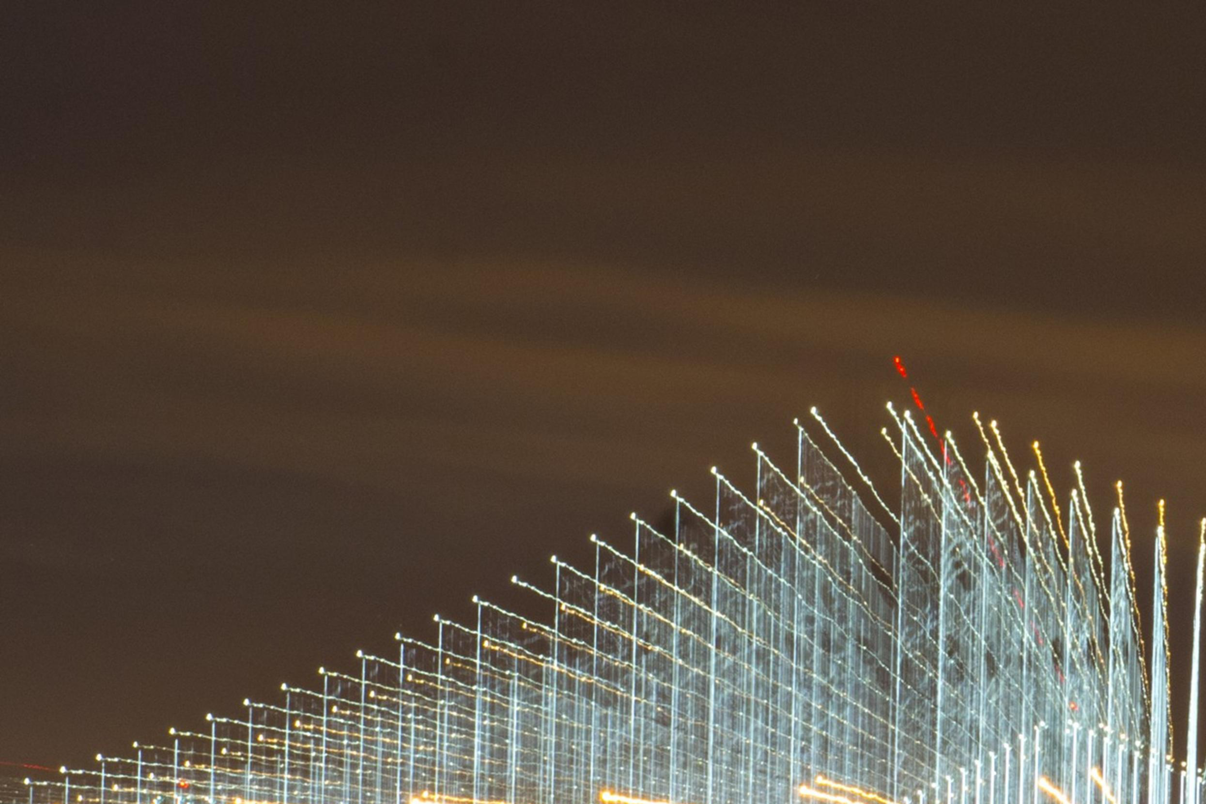 A light show illuminating cables on a suspension bridge shine at night.