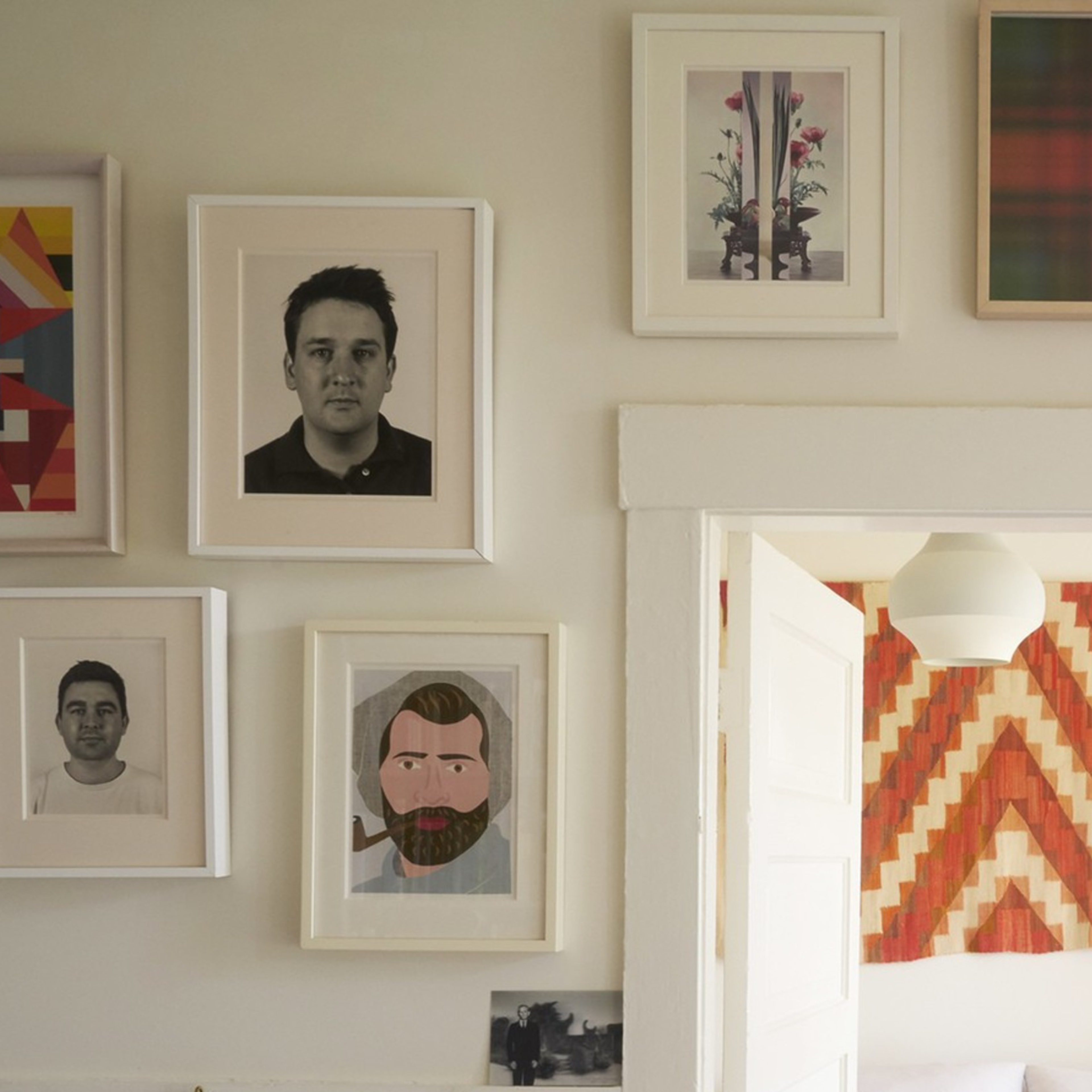 A cozy room with art on the walls, a door leading to a bedroom with a patterned decoration, shelves with files and books, and bags hanging on the walls.