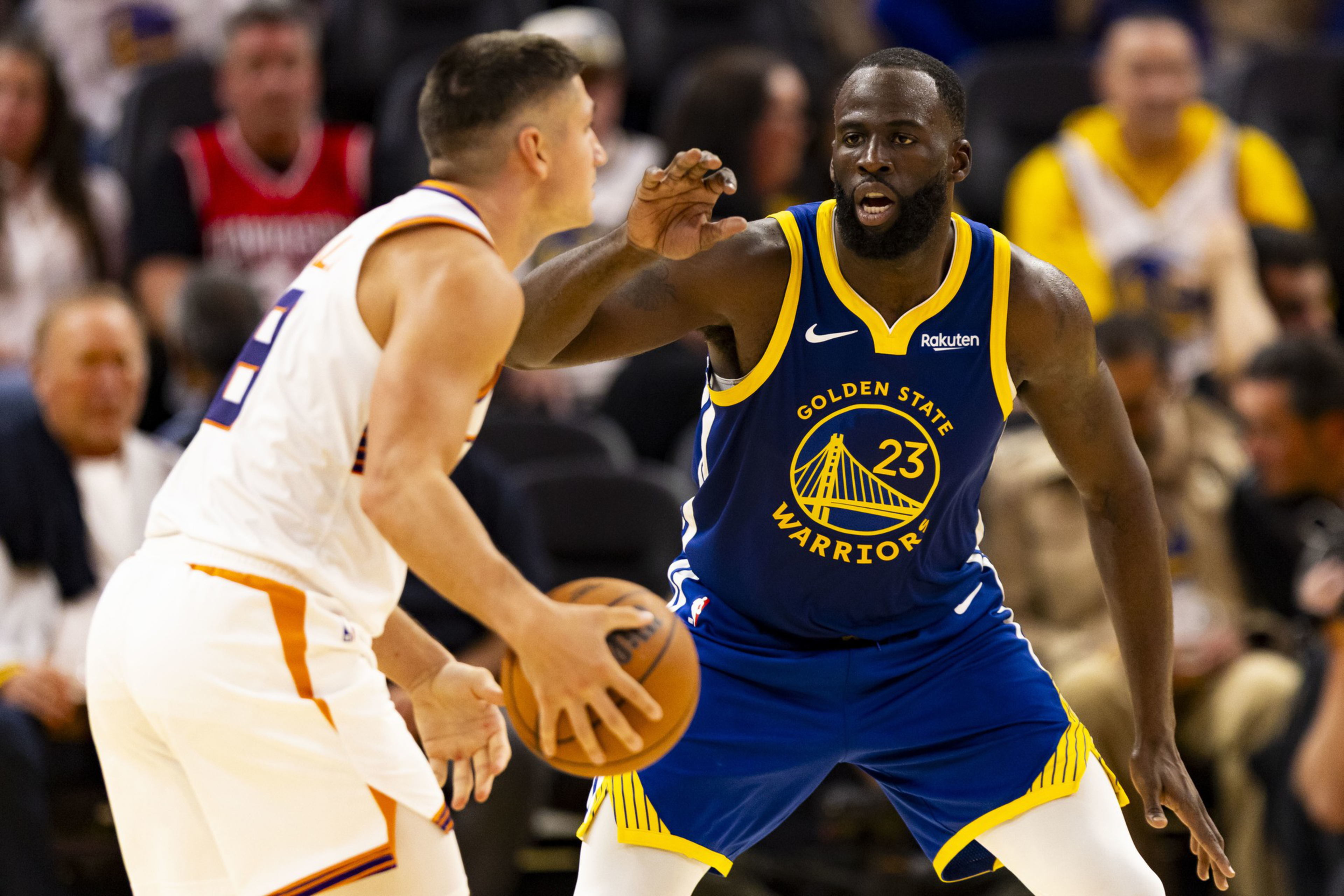 A Golden State Warriors player, wearing number 23, defends closely against a Phoenix Suns player holding a basketball during a game.