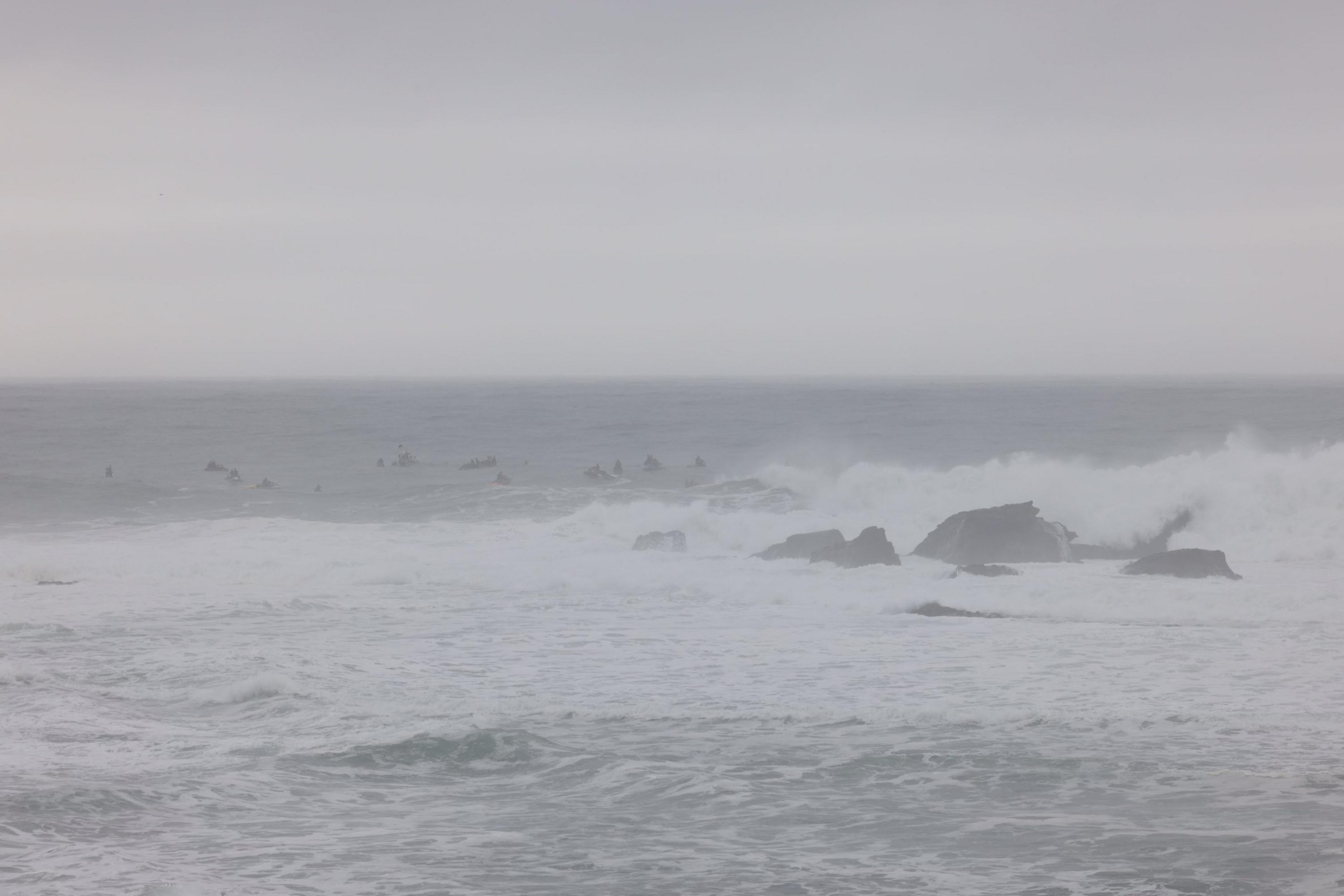 Ski boats can be seen in the distance as surfers wait to catch waves. 