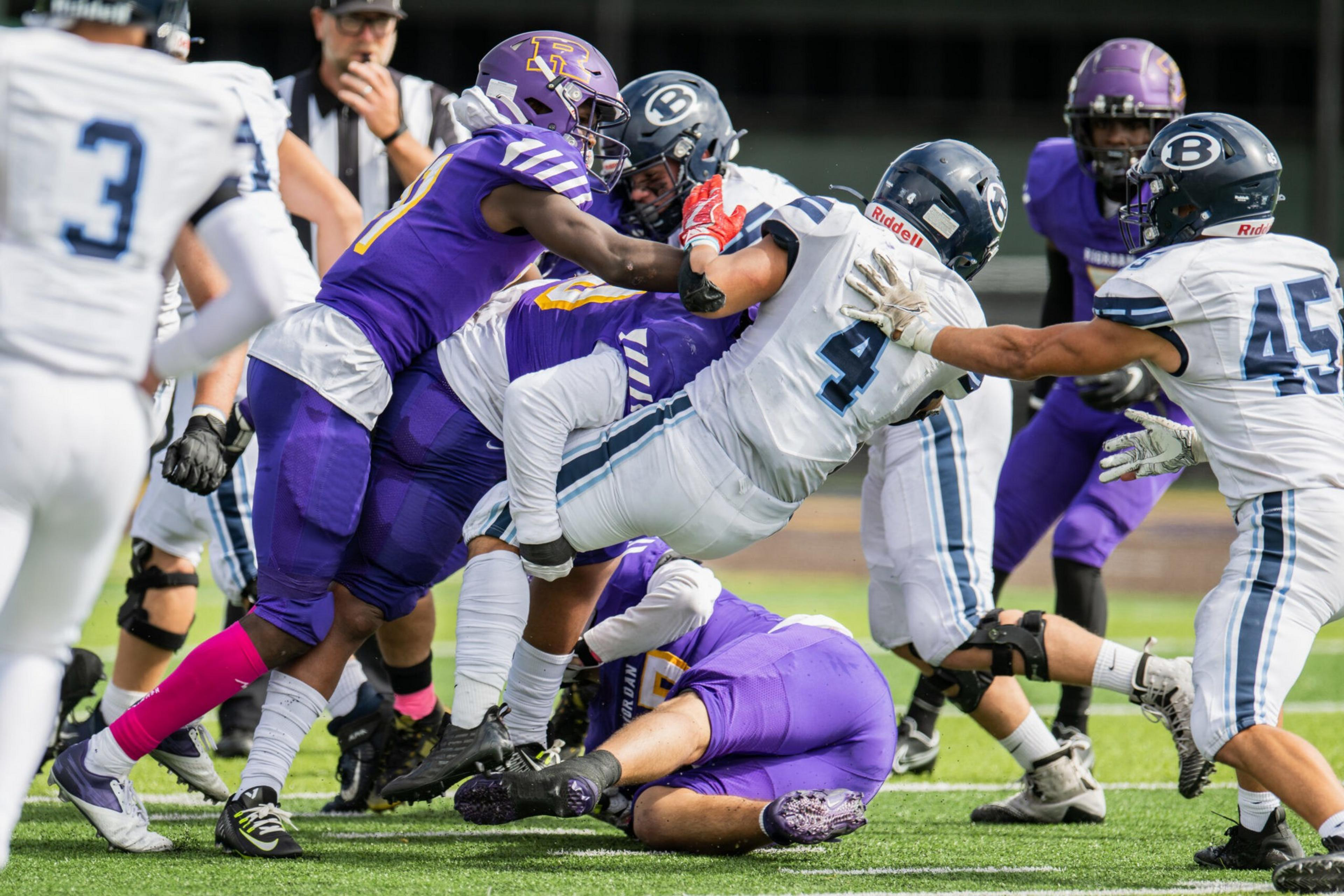 A football player in white jersey number 4 is tackled mid-air by players in purple jerseys during a game on a green field.