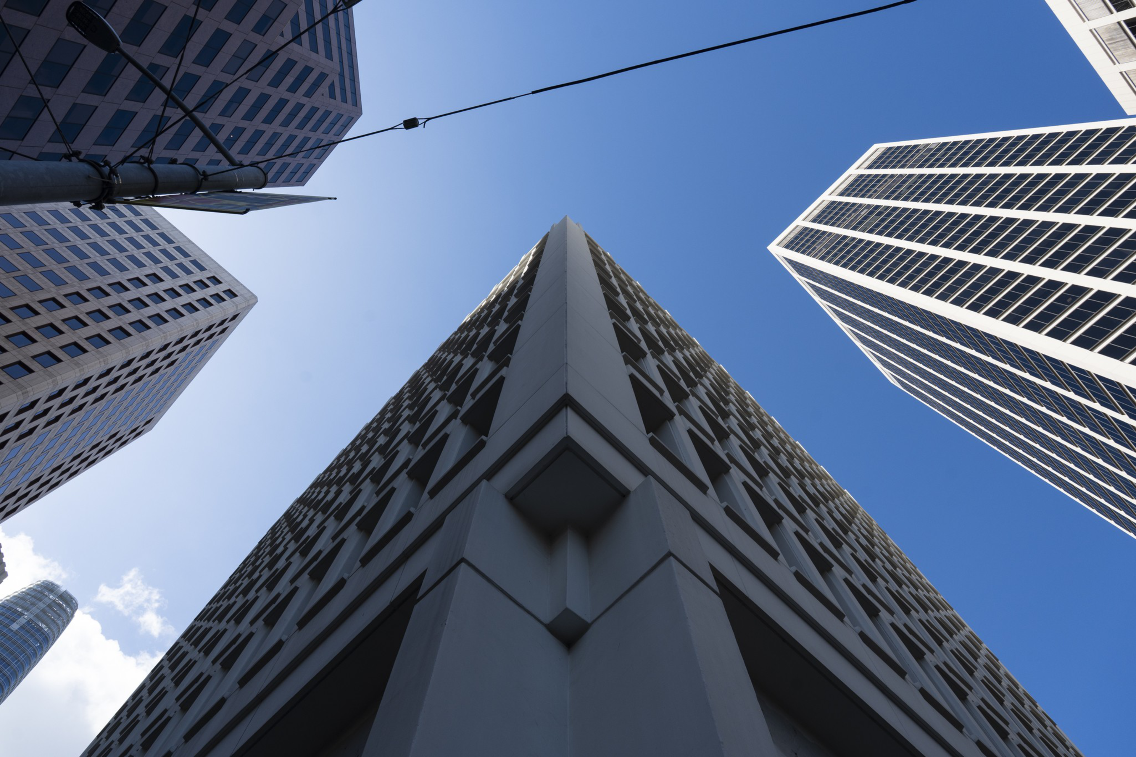 Tall skyscrapers with various window designs converge toward a clear blue sky, viewed from a sharp upward angle at the corner of one building.