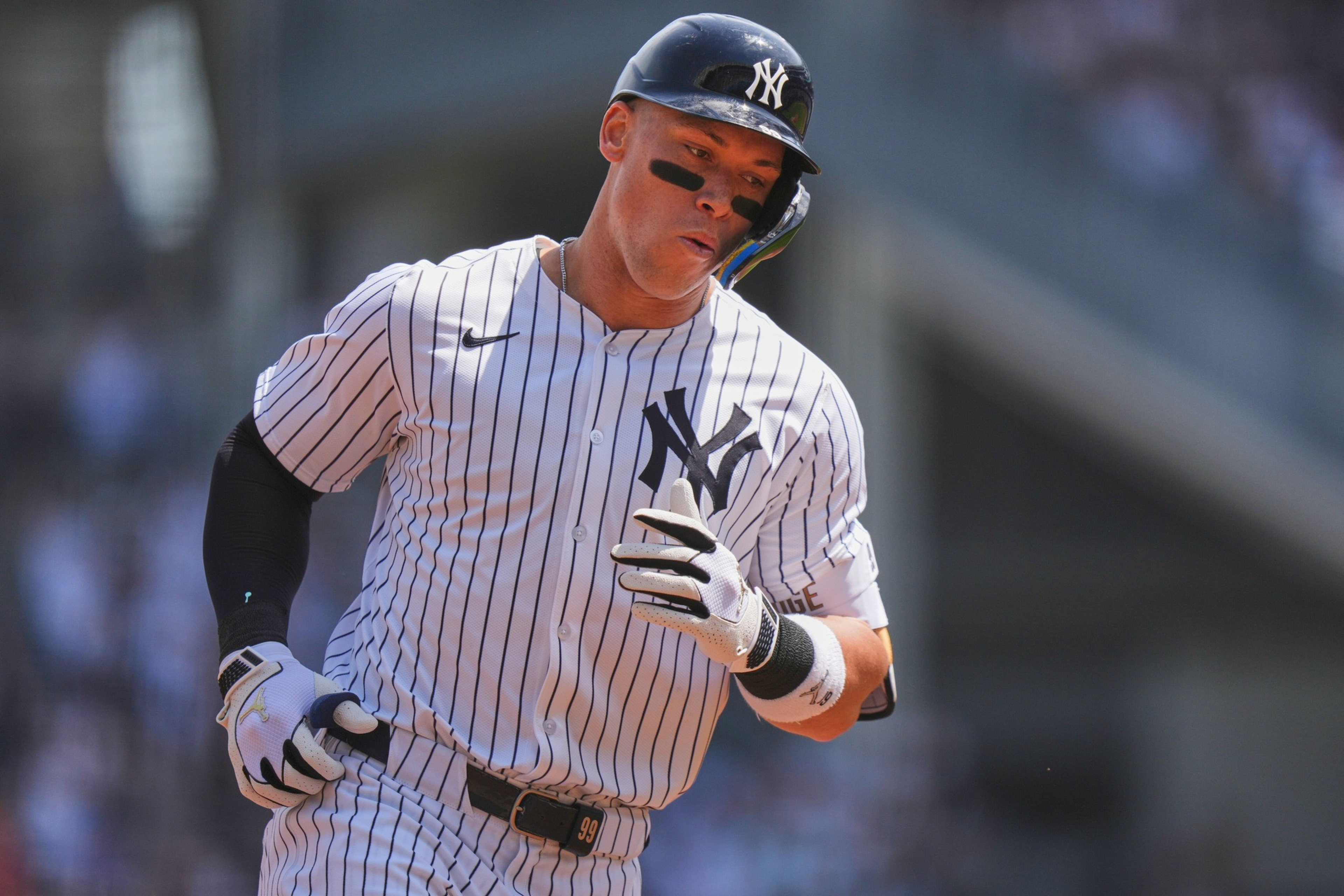 A baseball player, wearing a pinstriped uniform and black helmet, is running. He has black eye paint and is in motion with a blurred background.