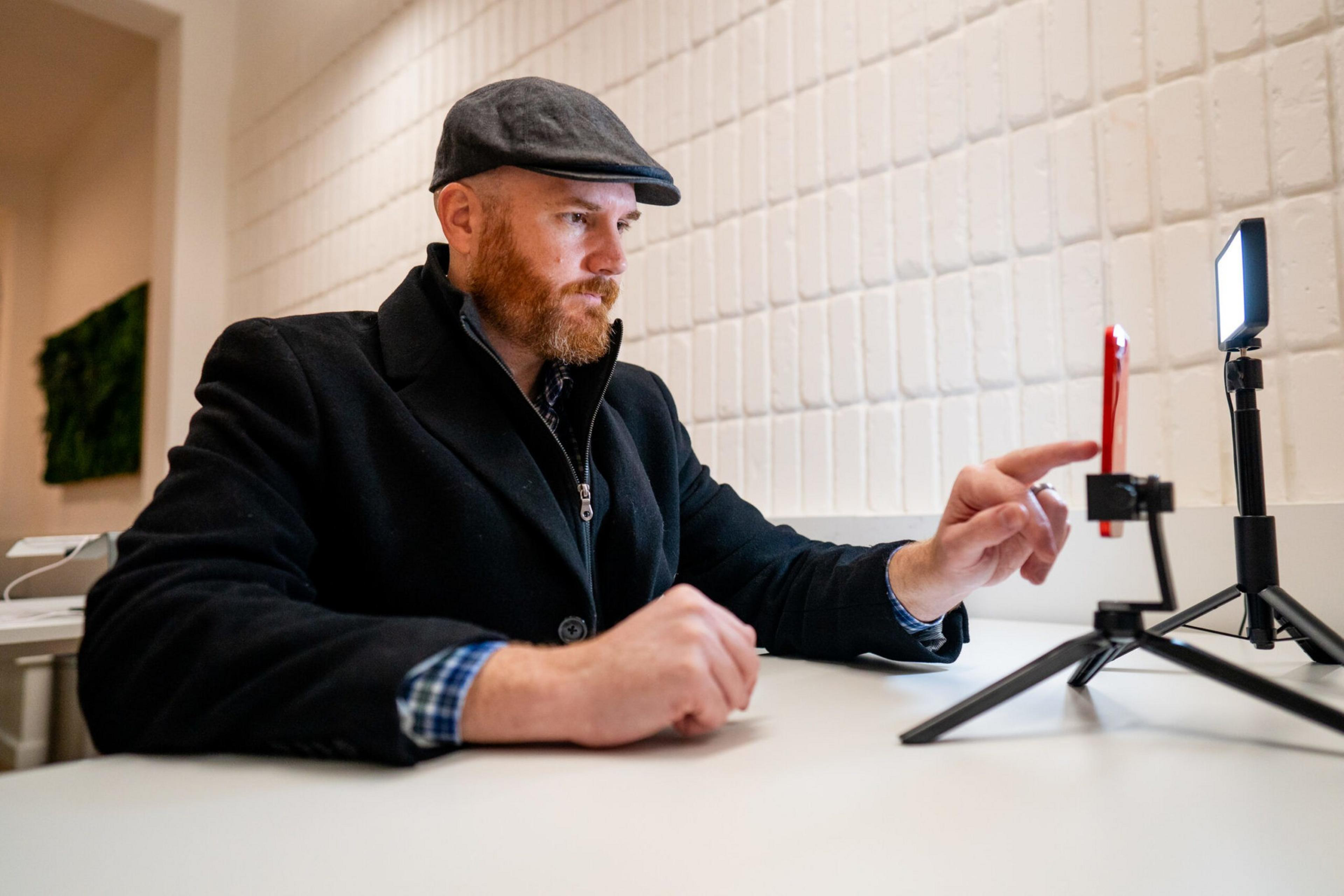A hatted man interacts with a smartphone mounted on a tripod.