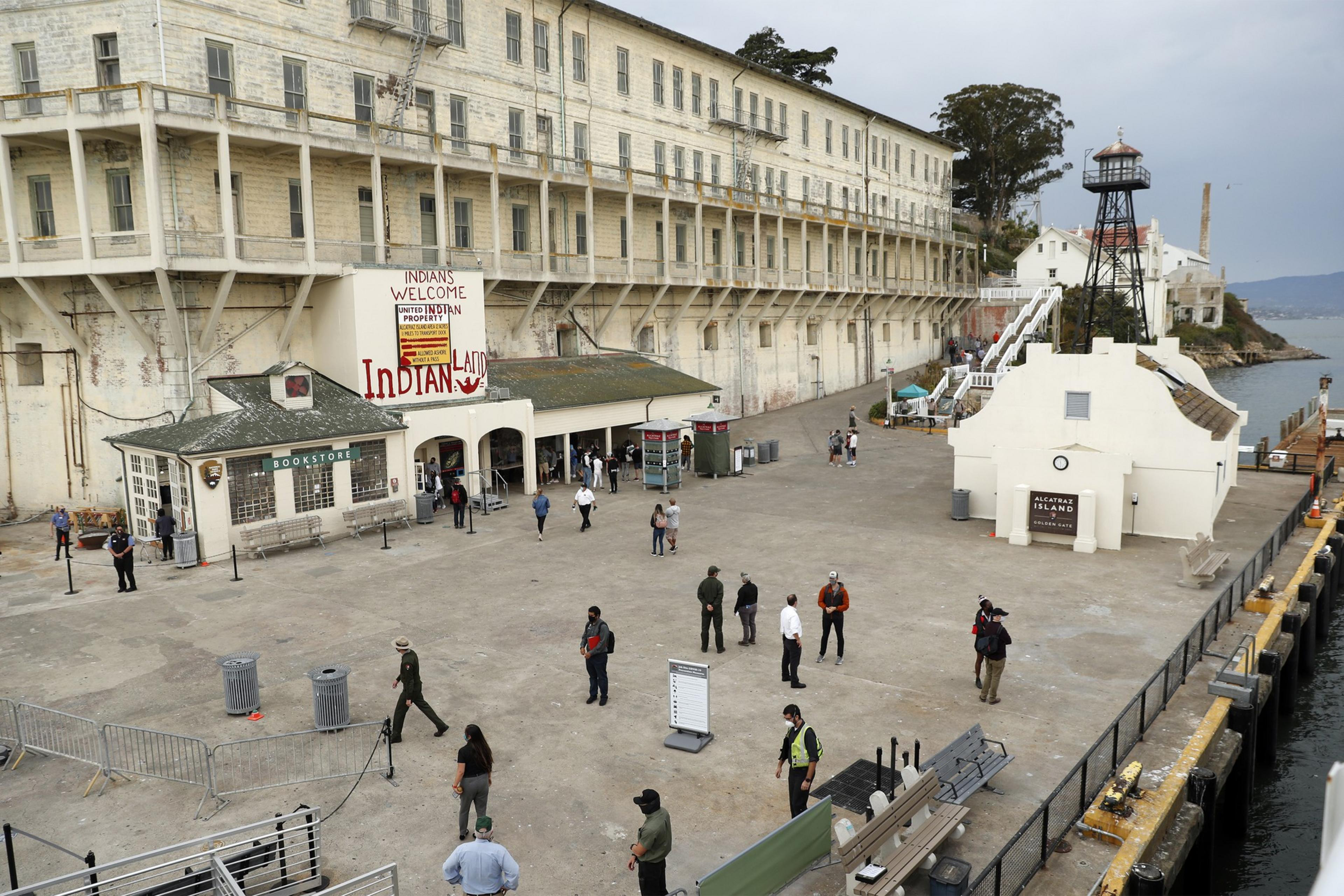 The image shows a large, old building labeled &quot;INDIAN LAND,&quot; with people walking on a concrete area in front. There's a lighthouse and Alcatraz signage nearby.