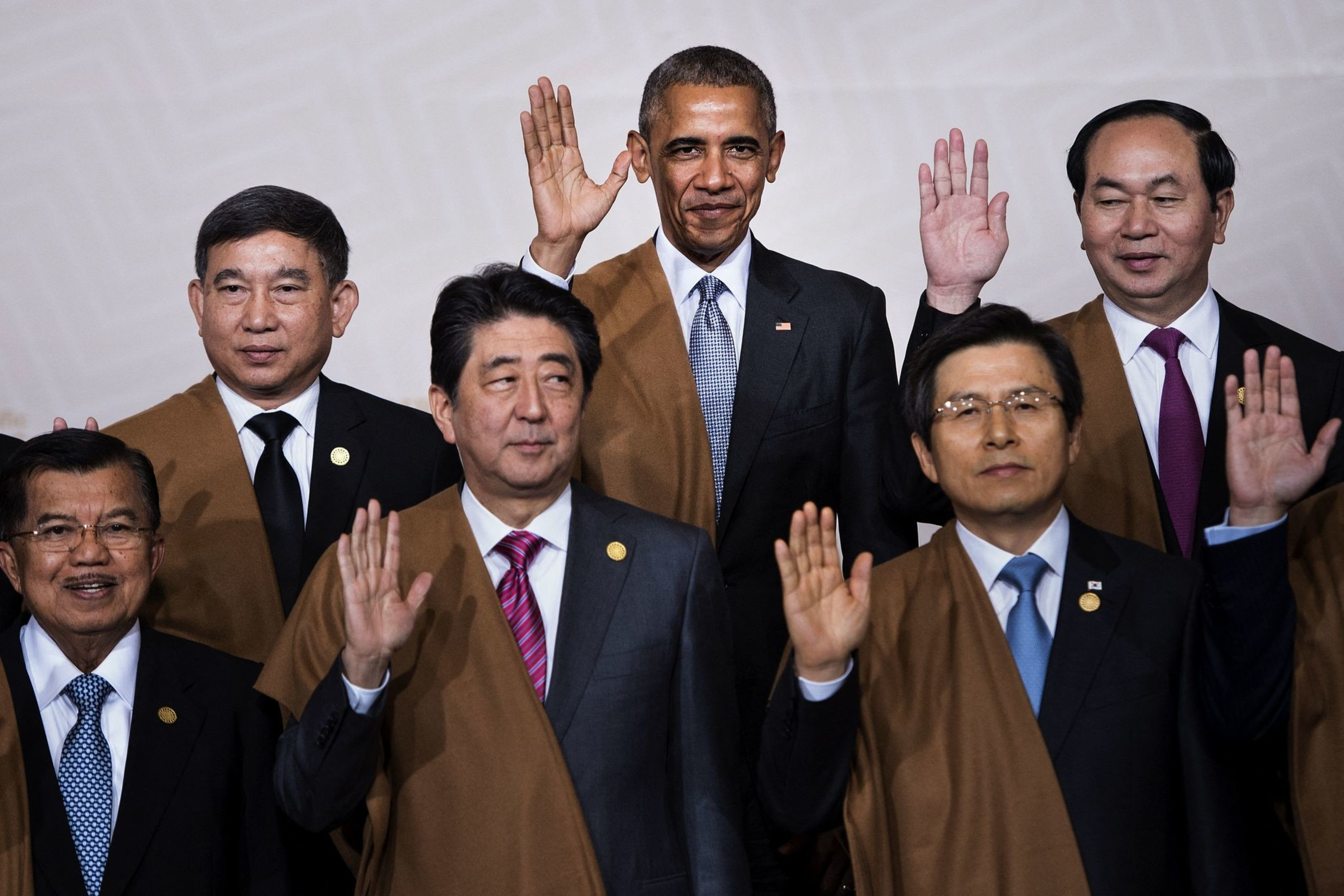 The world leaders are standing together in traditional Peruvian attire with their hands raised for a portrait.