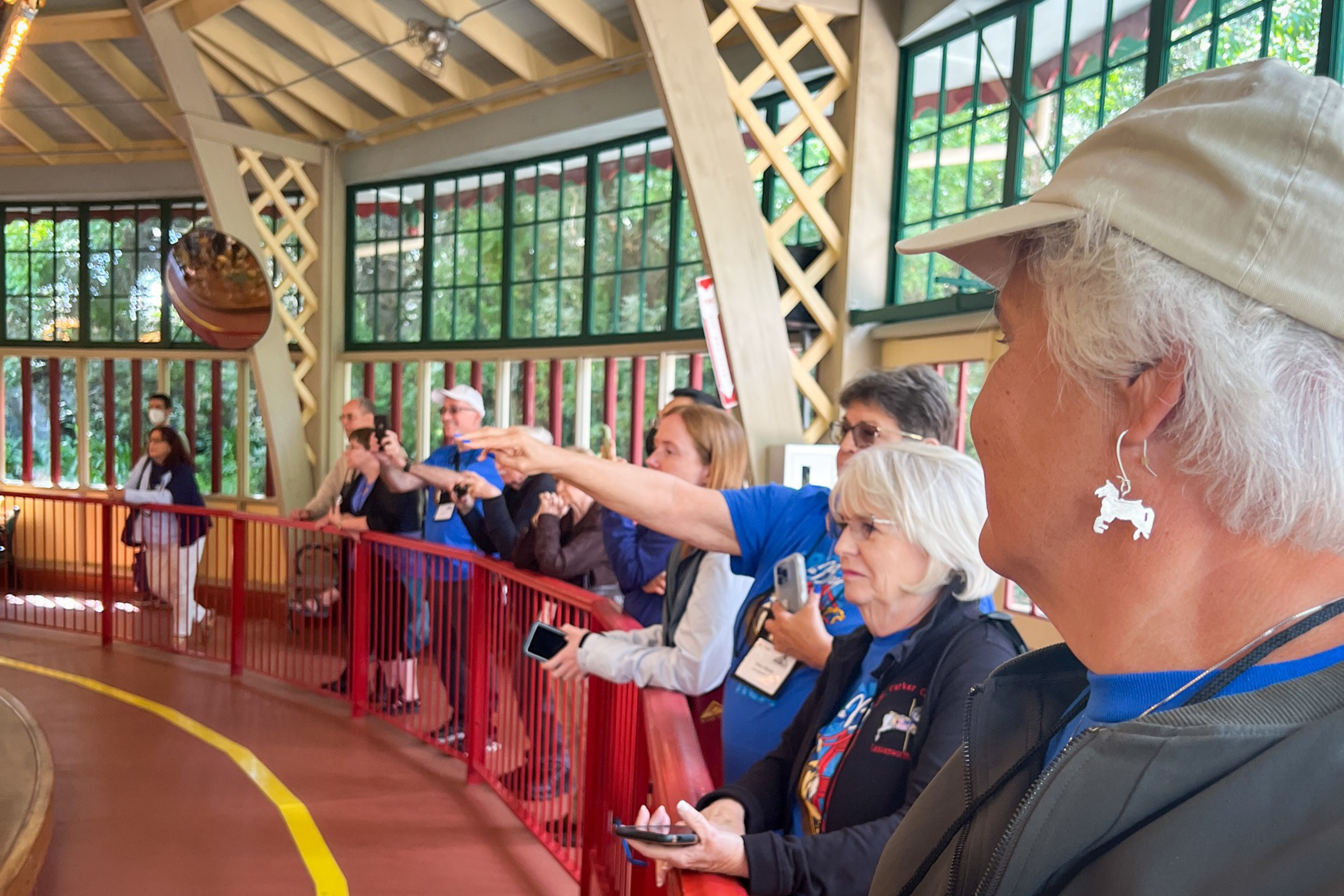 A group of people stand behind a red railing inside a glass-paneled building, watching and pointing at a large silver ball suspended in the air.
