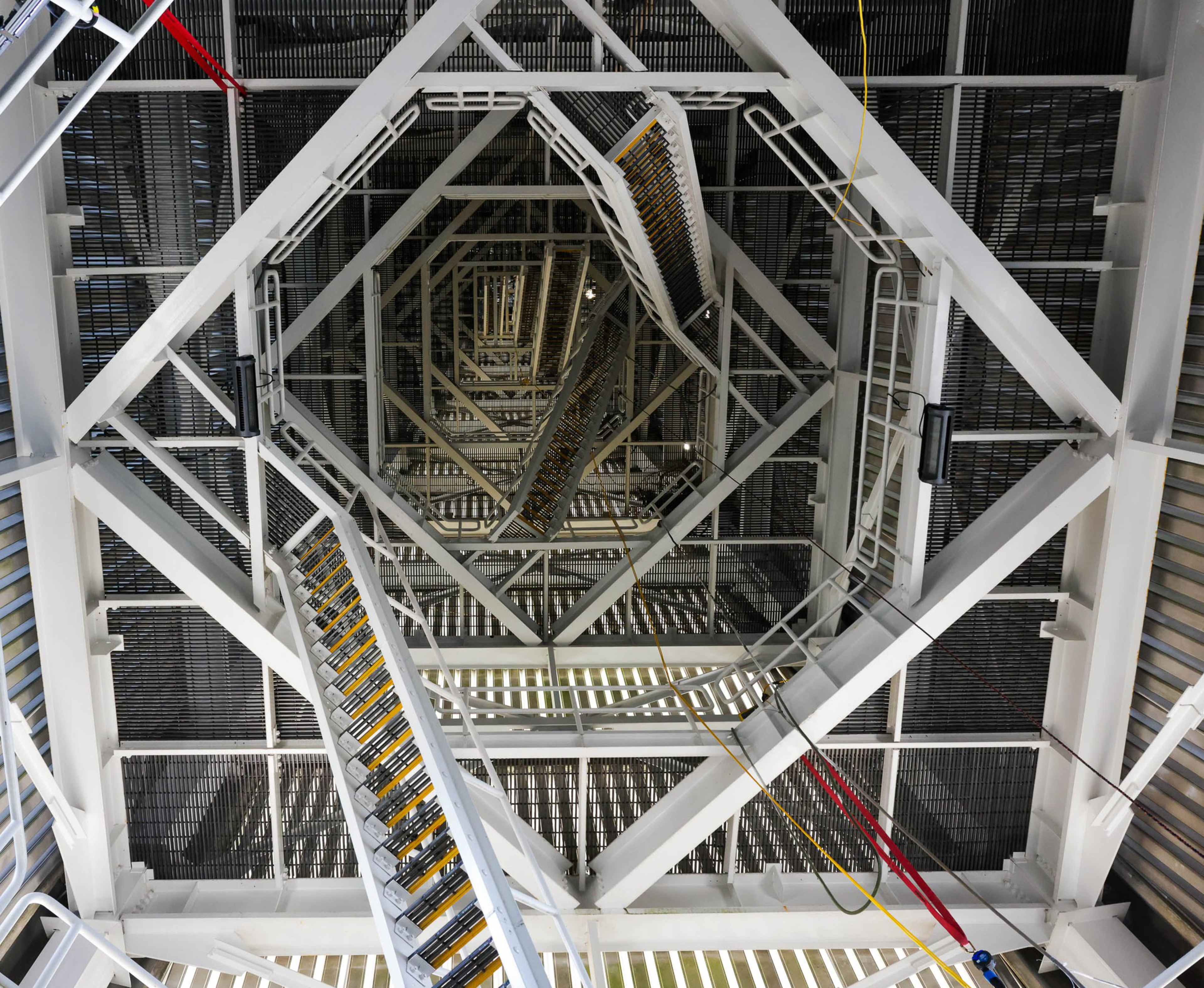 Looking down a complex, geometric stairwell with metal railings and steps amidst white support beams.