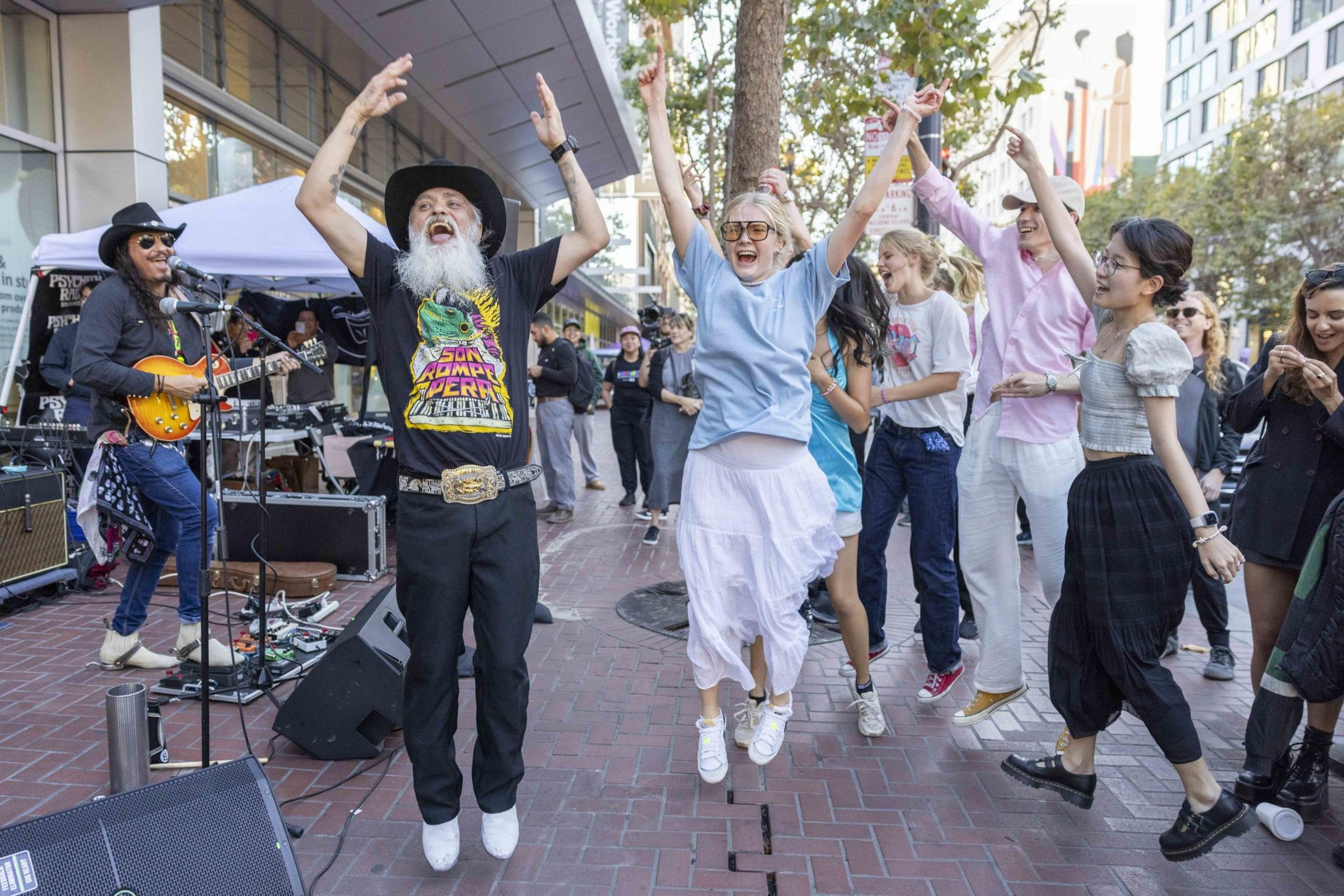 A lively street performance with a guitarist and a group of people joyfully dancing and jumping in unison, capturing a vibrant and energetic moment.