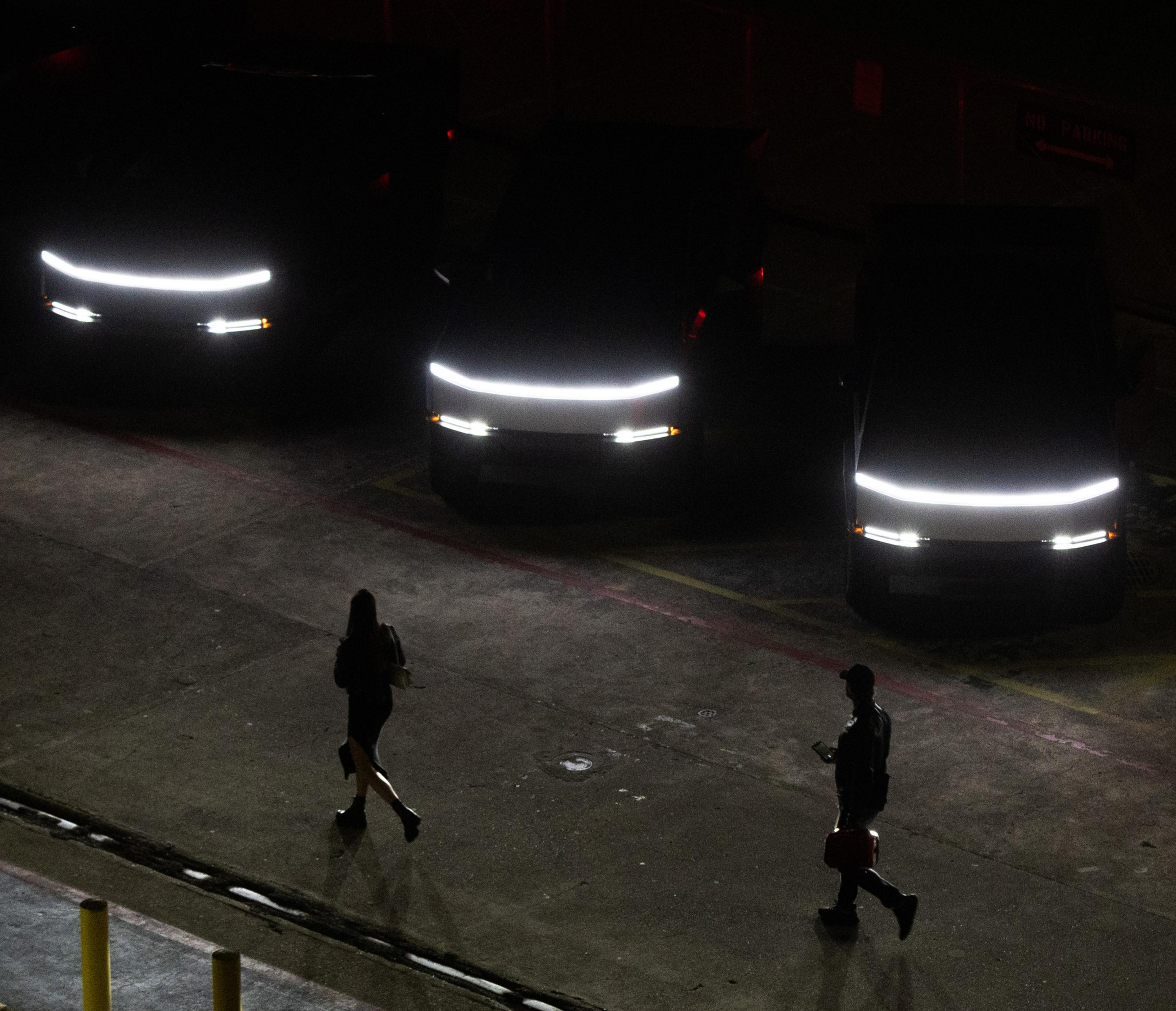Pedestrians walk past Tesla Cybertrucks’s parked in a line at the SF Deep Tech Week launch party on the USS Hornet aircraft carrier in Alameda on Sunday, June 23, 2024. The event includes tech showcases, demos and a rave. The USS Hornet is retired and operates as a sea, air and space museum.