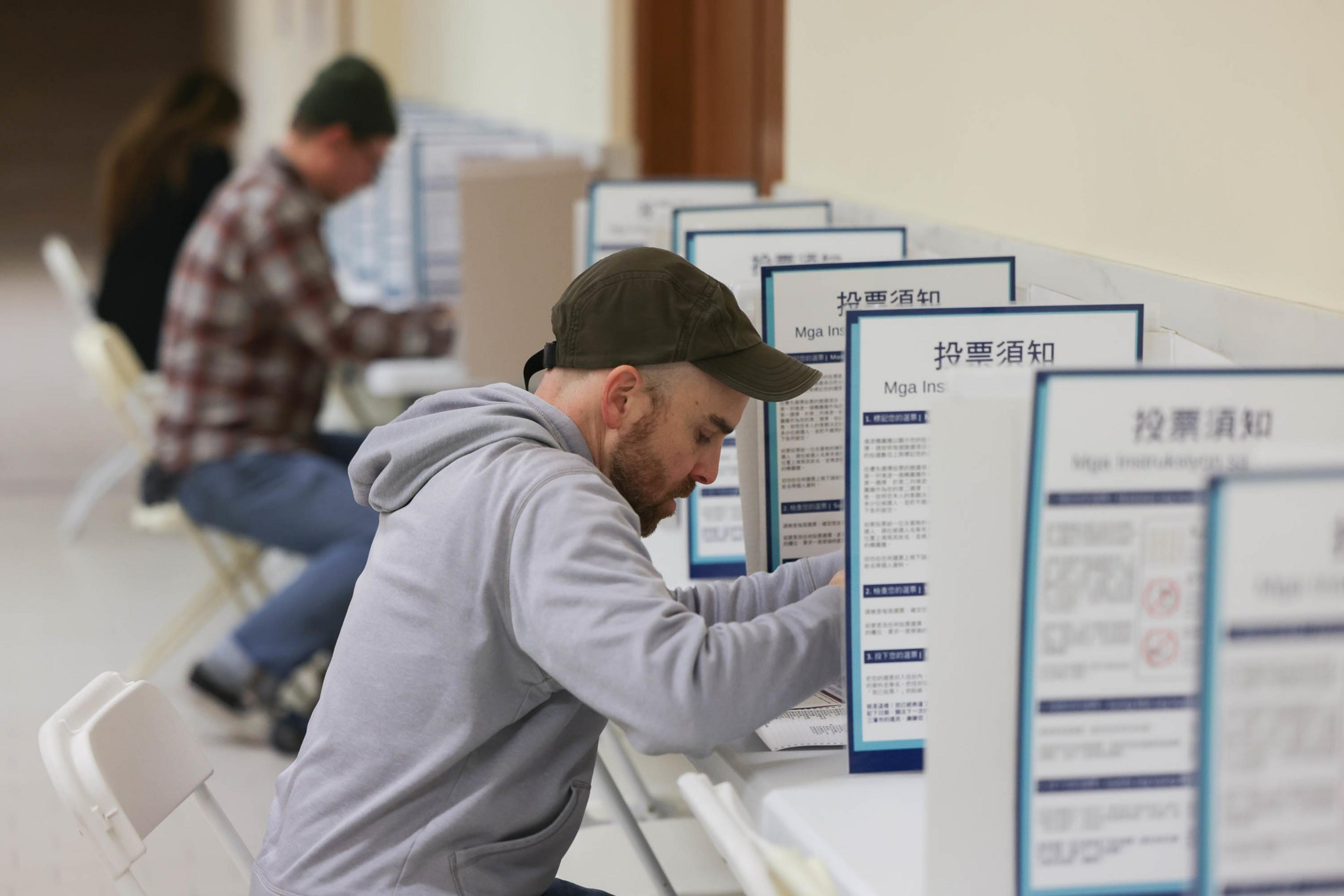 People are seated at booths, filling out documents, with privacy dividers displaying text in multiple languages.