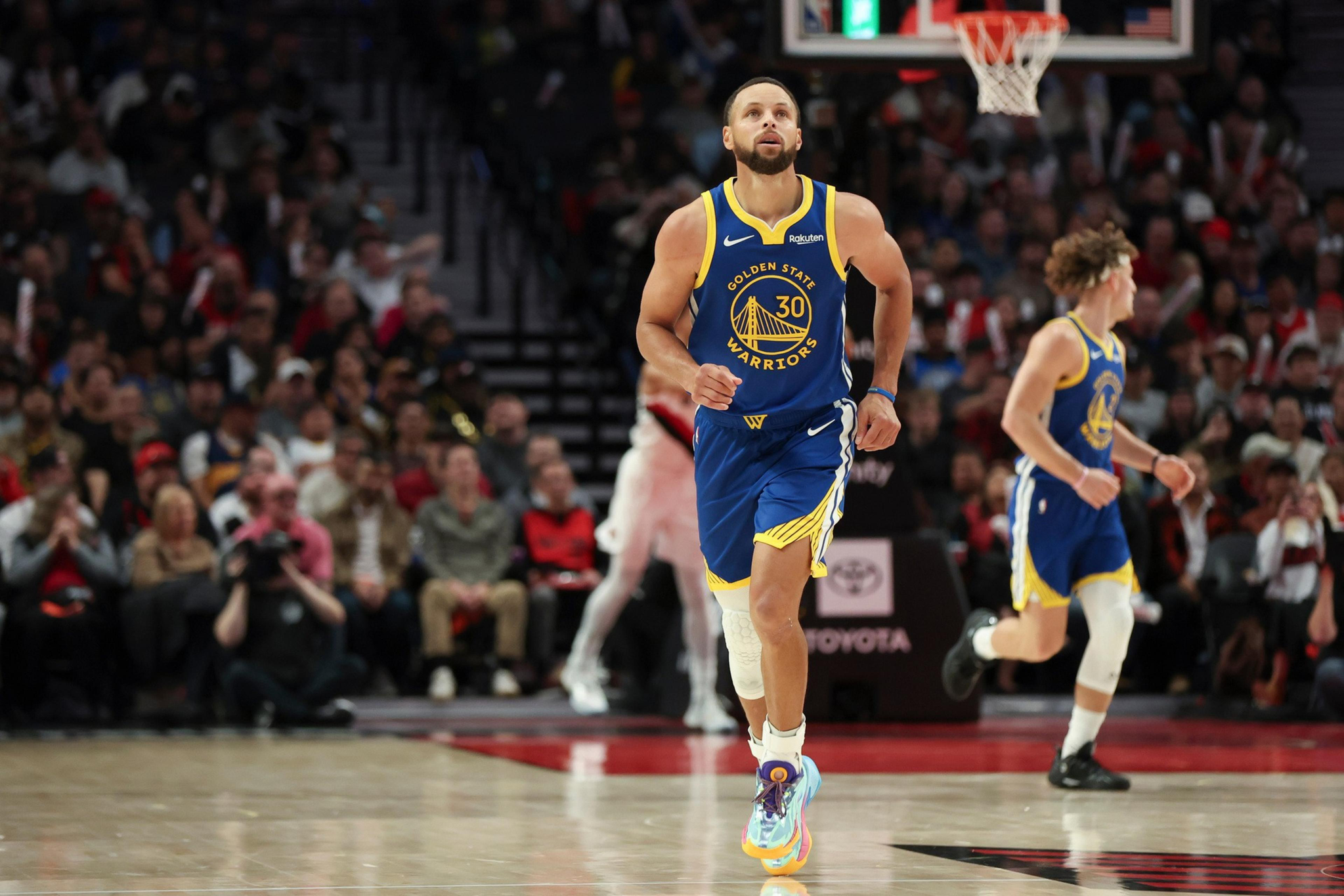 A Golden State Warriors player wearing jersey number 30 runs on the basketball court with a teammate and audience in the background.