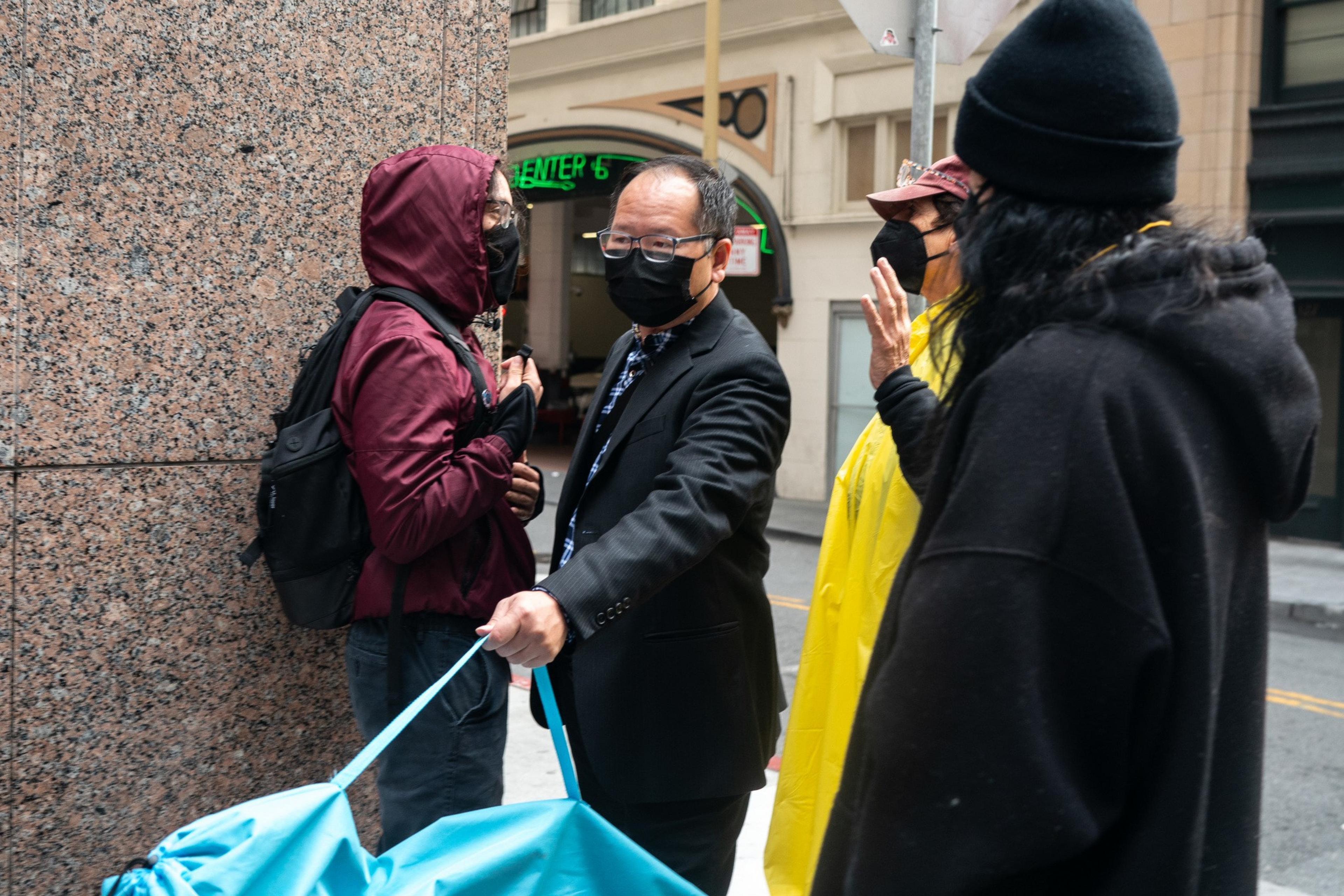 A man in a suit walk along a sidewalk through a few protesters trying to obstruct his path.