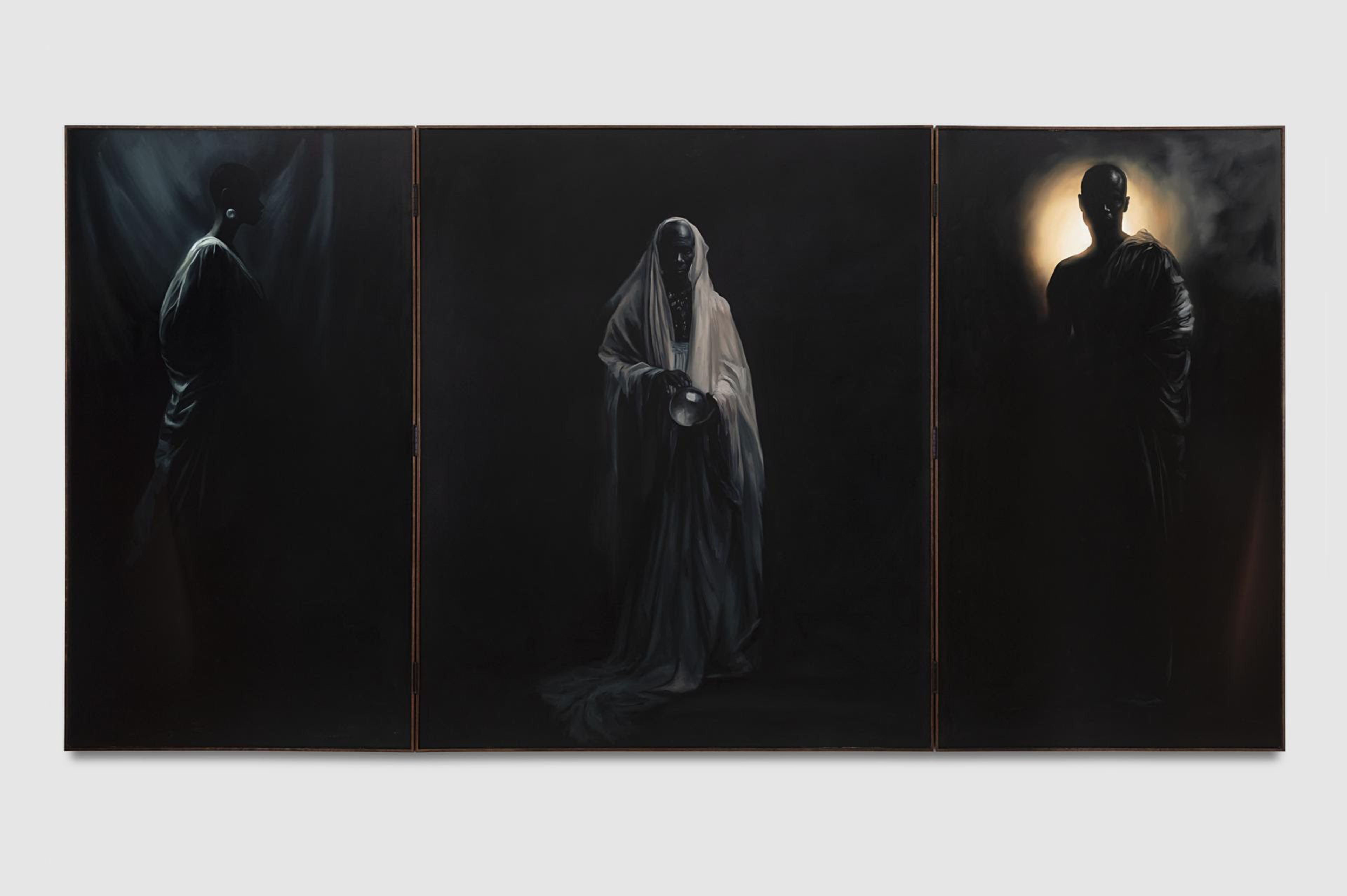 Three dark, shadowy figures draped in robes stand against a black background, with faint light highlighting their faces and hands.