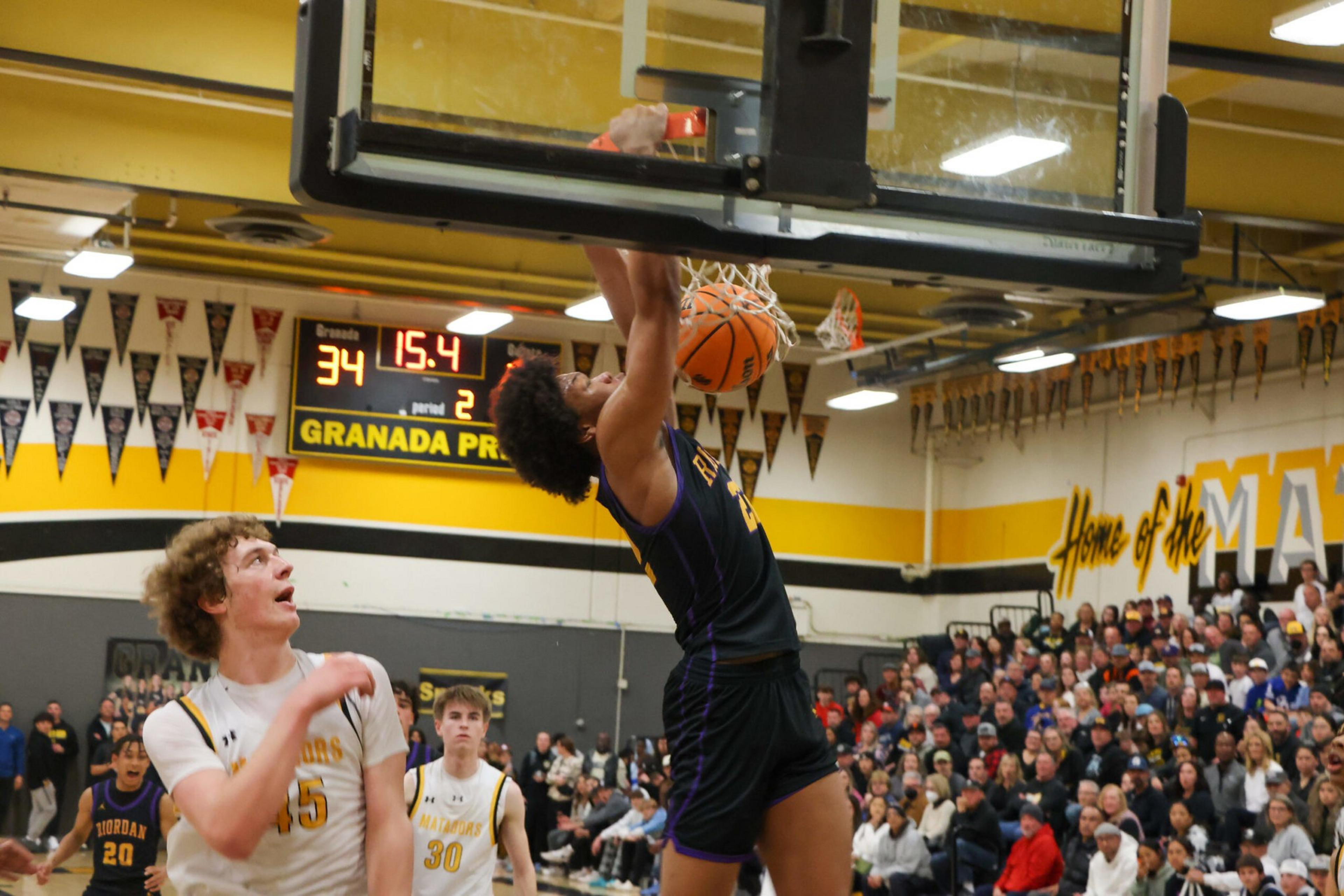 A basketball player in a black uniform dunks the ball while a player in a white uniform watches; the scoreboard reads 34-15.4 in the second period.