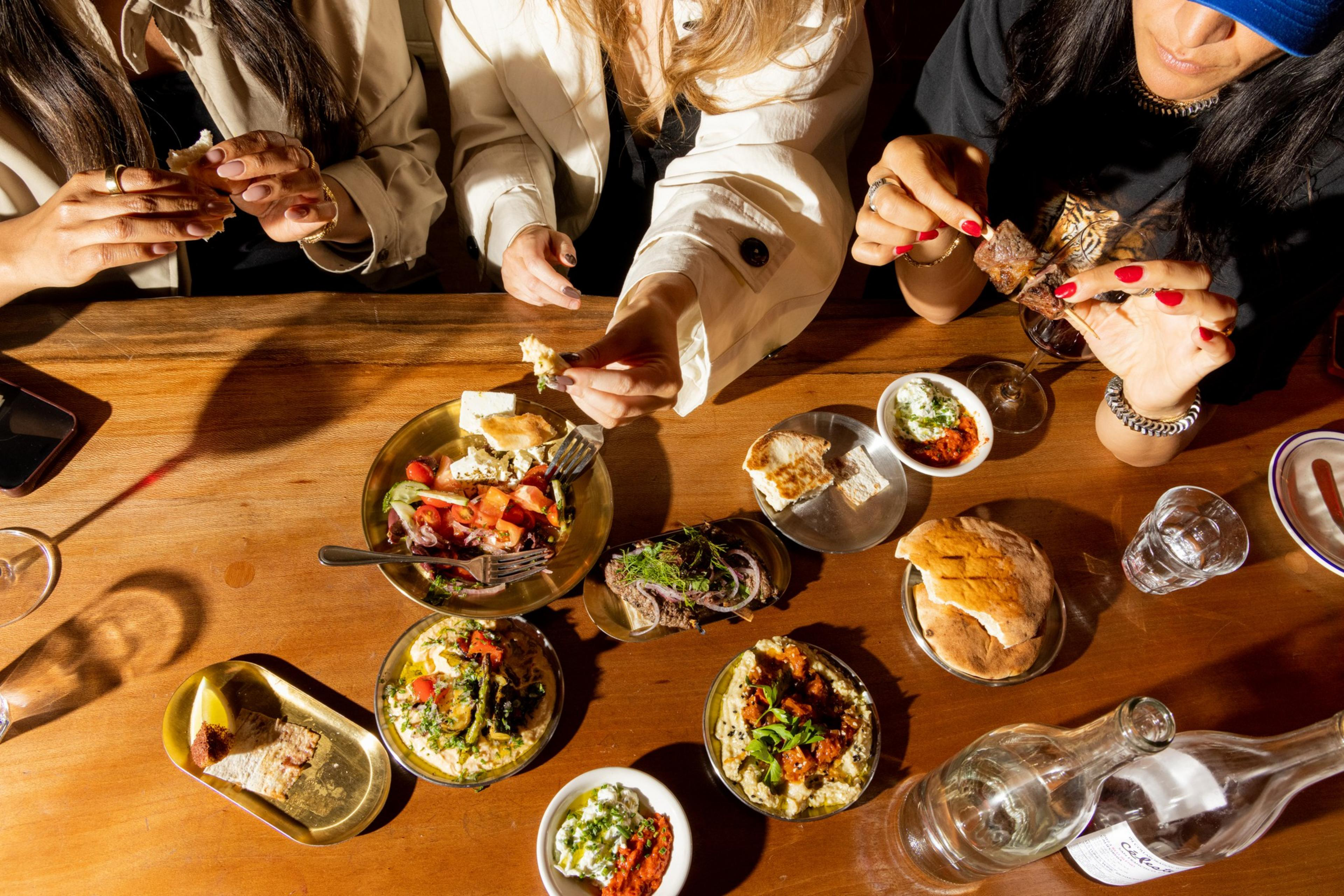 An overhead view of a bar loaded with small plates of food and glasses of wine.