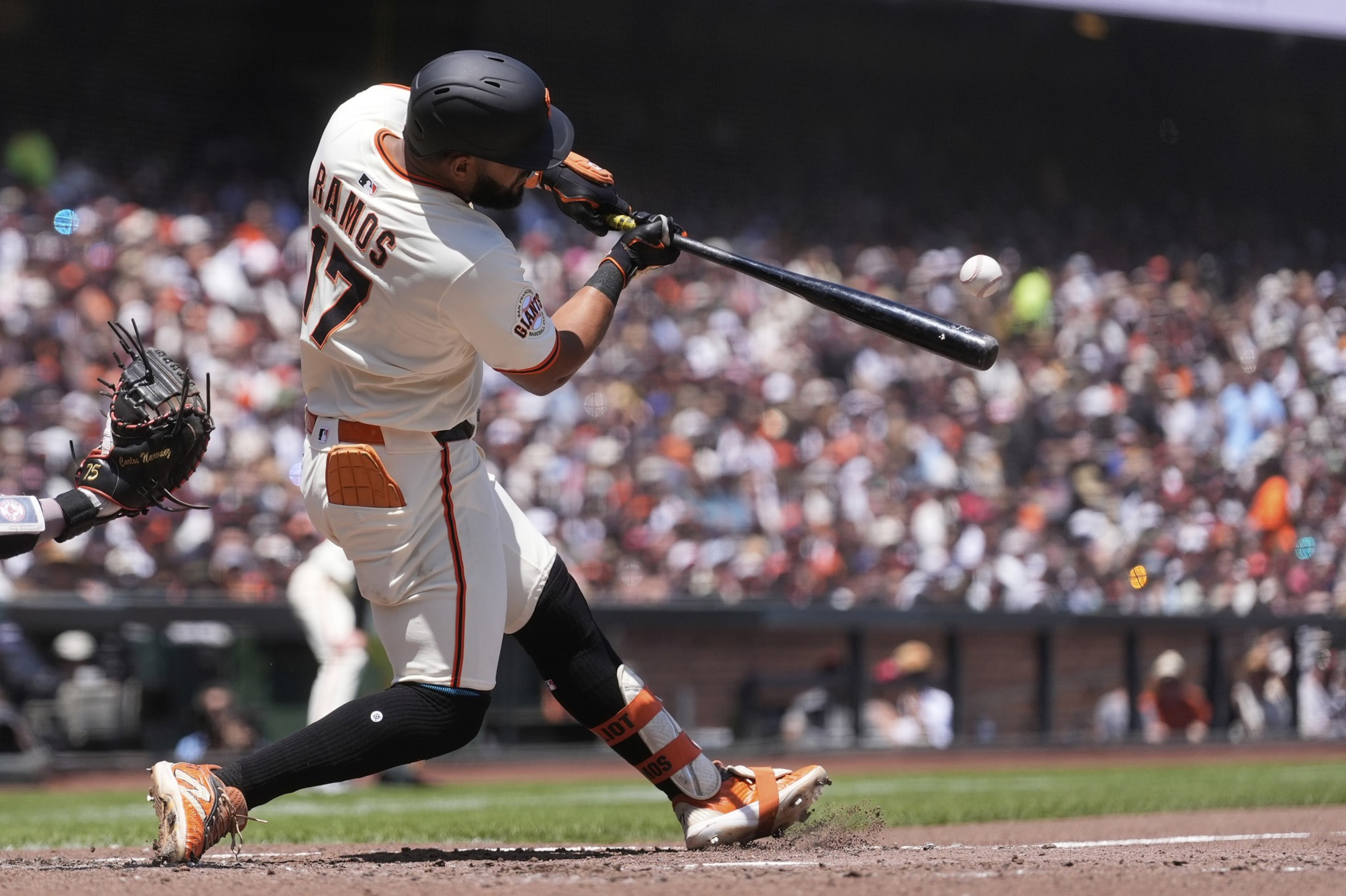 A baseball player in a white uniform and black helmet is mid-swing at a baseball. The crowd in the background is blurred, adding focus to the action.