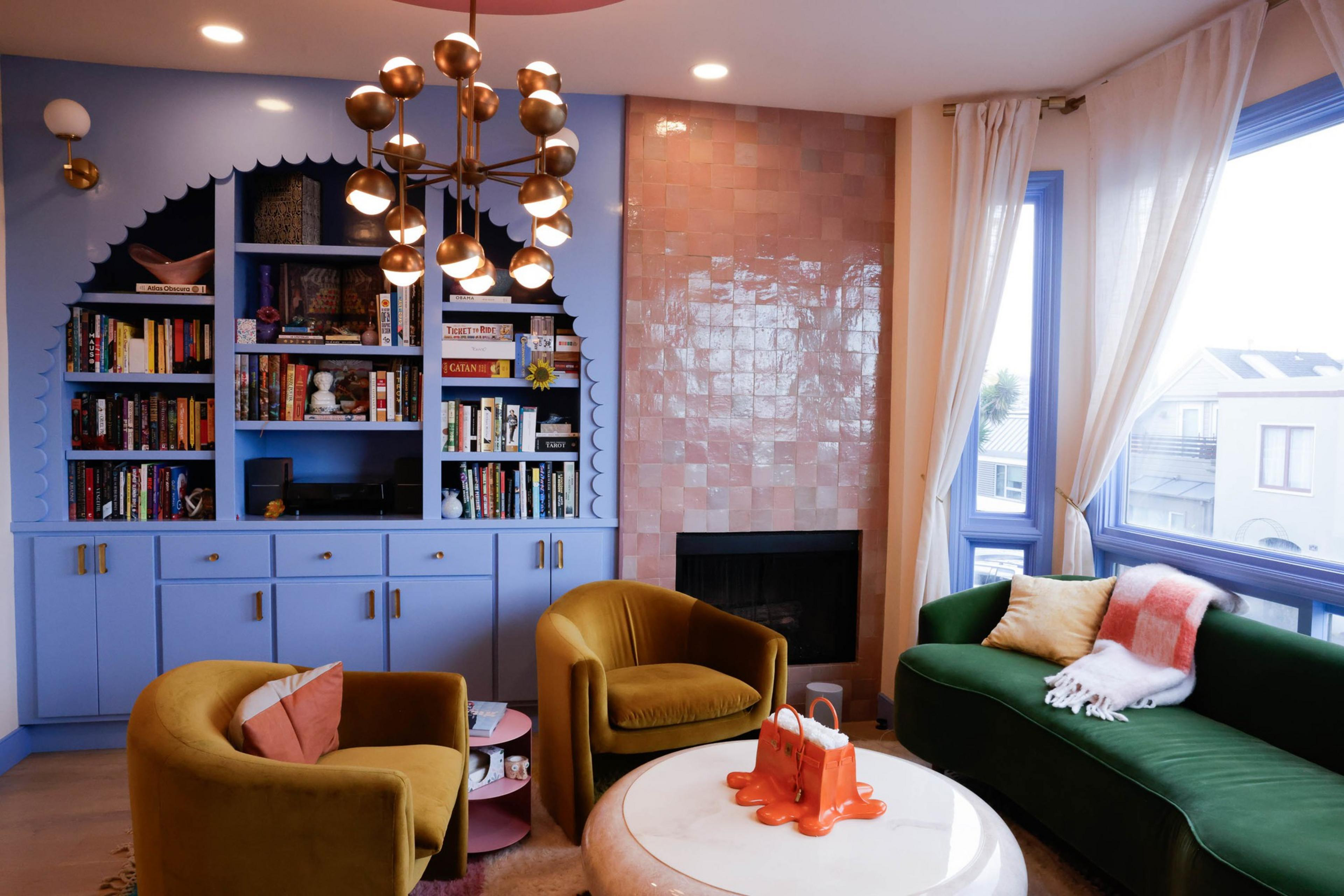 San Francisco's Floral House features a blue scalloped custom bookcase, a green velvet couch, yellow velvet armchairs and a tiled pink fireplace wall.