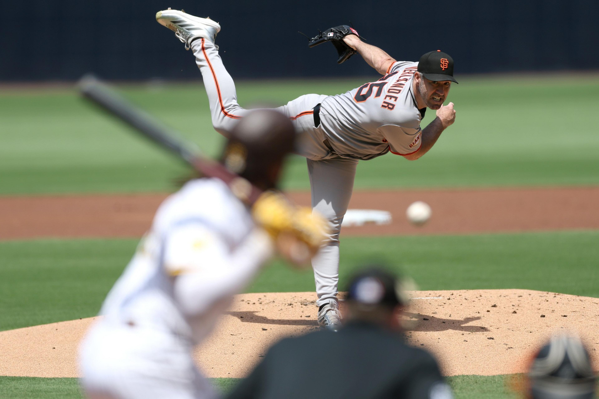 A baseball pitcher in a San Francisco Giants uniform throws a pitch toward a batter in a white uniform, with the ball mid-air.