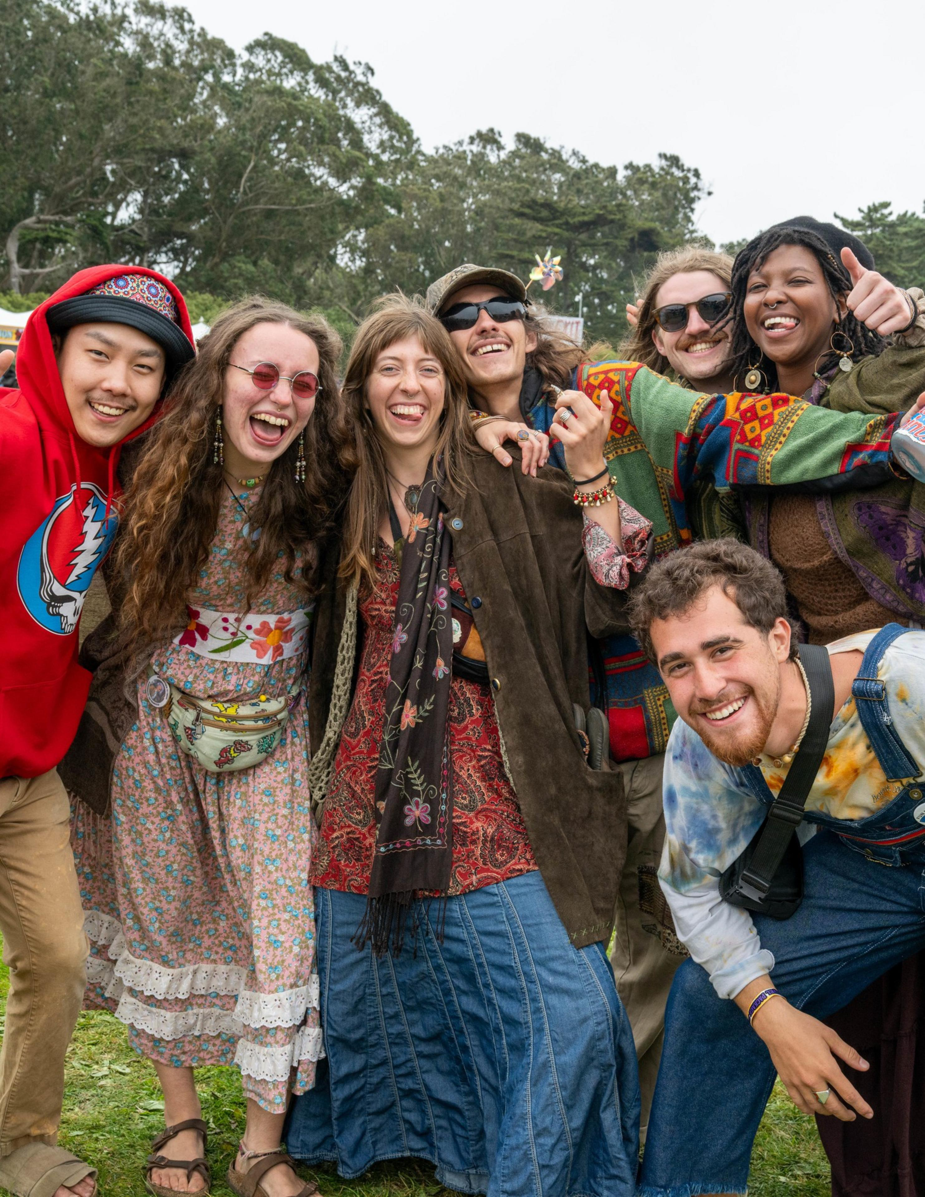 Six people dressed in colorful, vintage, and bohemian clothing smile and pose closely together outdoors, radiating joy and friendship.