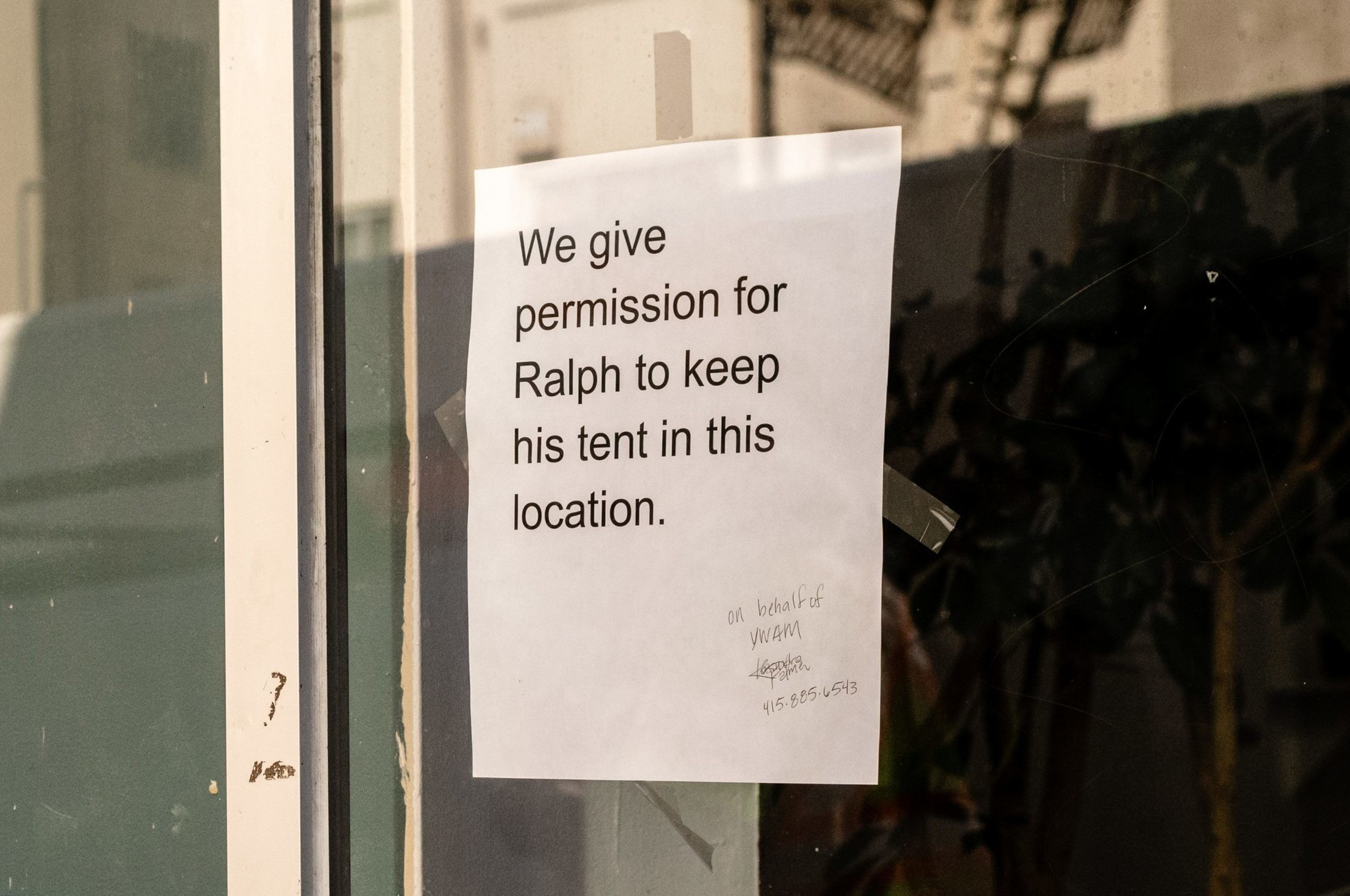 A sign in a window that reads, &quot;We give permission for Ralph to keep his tent in this location&quot;. 