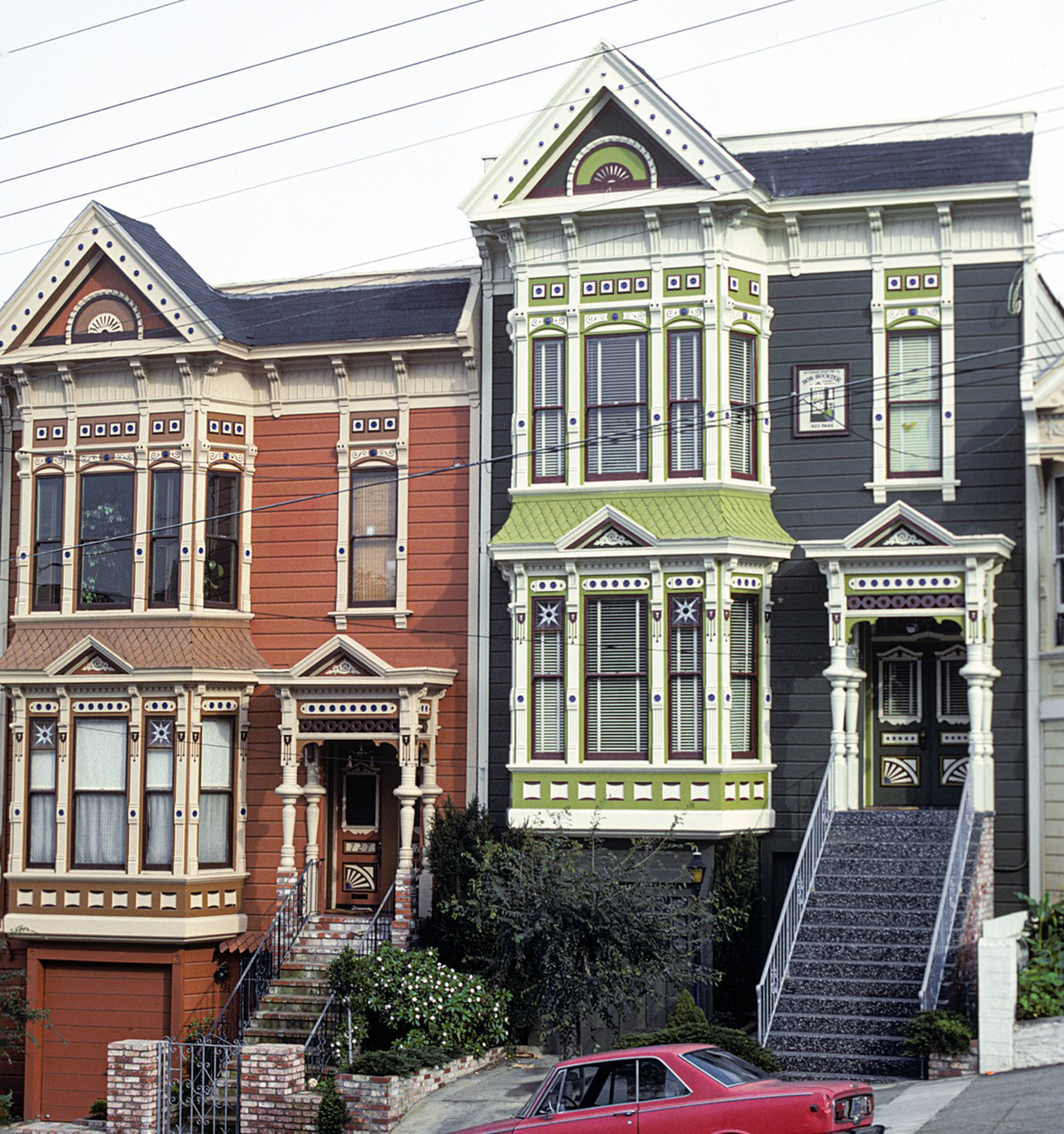 Two Victorian-style houses are shown, one painted red with cream trim and the other dark gray with green and white detailing, with a red car parked in front.