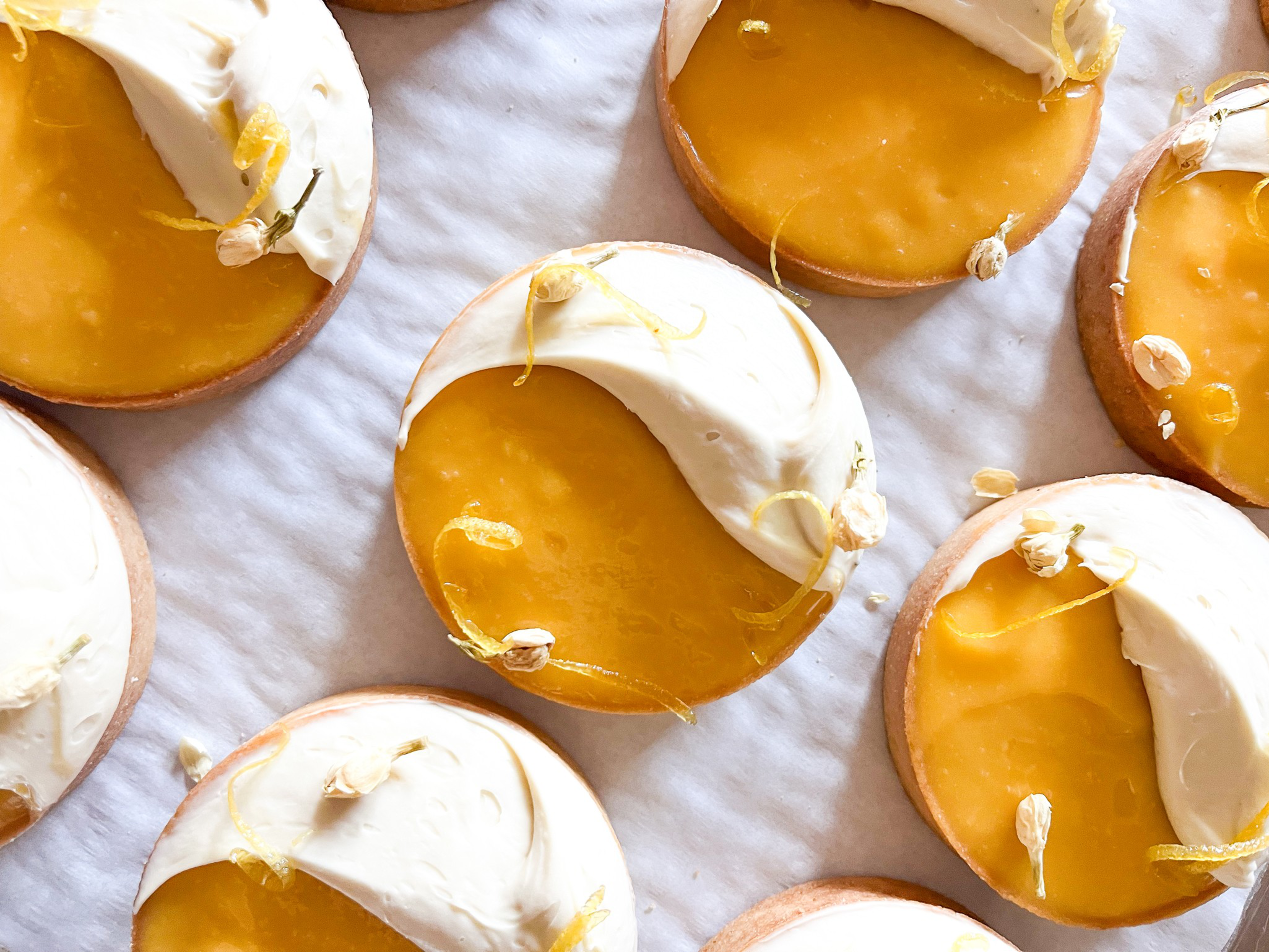 Round cookies topped with half yellow-orange glaze and half white frosting, garnished with small flower petals and thin yellow strands.