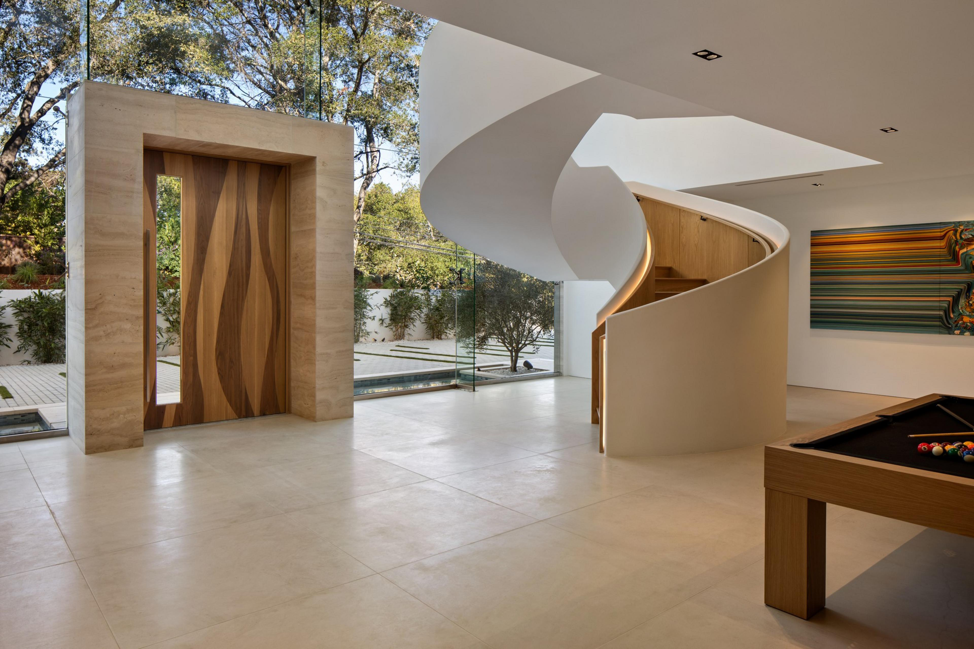 A modern indoor space features a wooden double door in stone framing, a white spiral staircase, a pool table, and a colorful abstract wall painting.