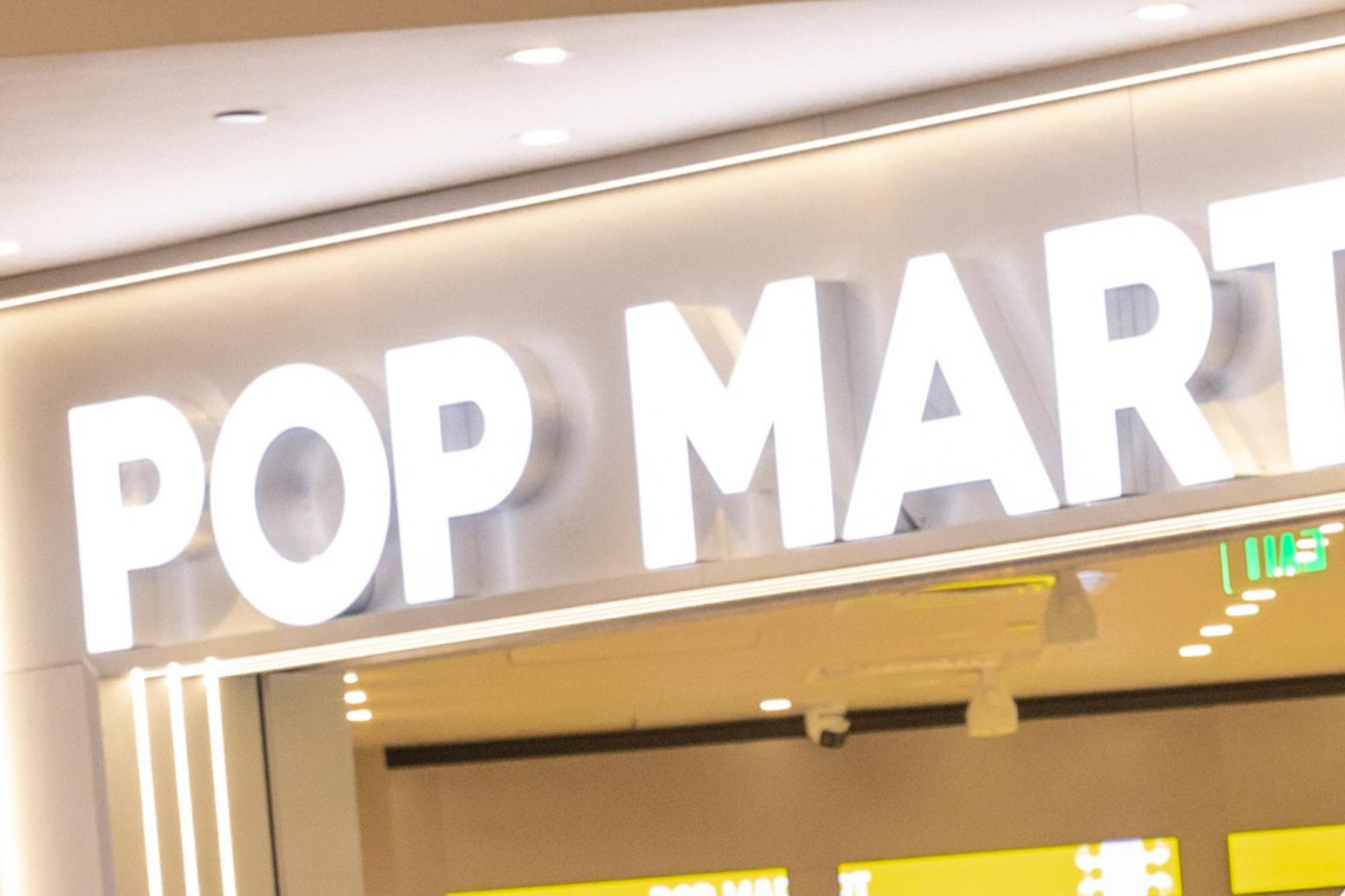 People are gathered in front of a store named "POP MART", with many looking at their phones while standing in line.