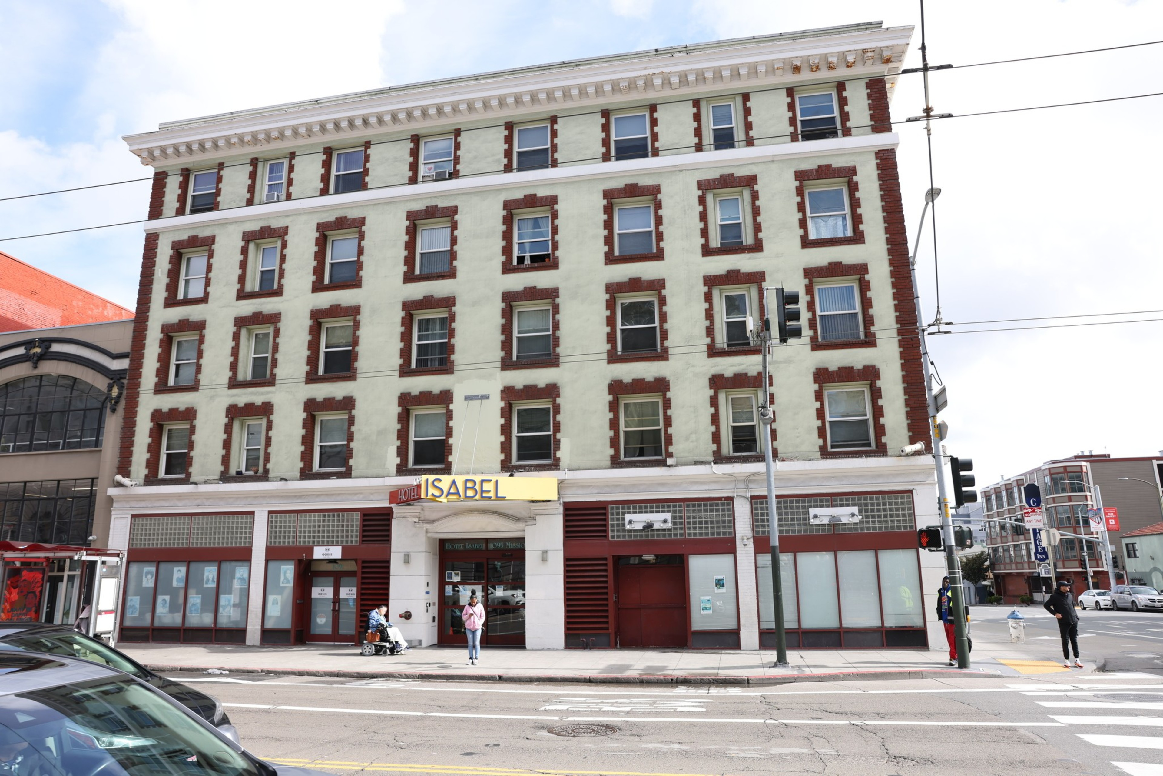 A four-story red and white building at a street corner with shuttered shops and pedestrians.