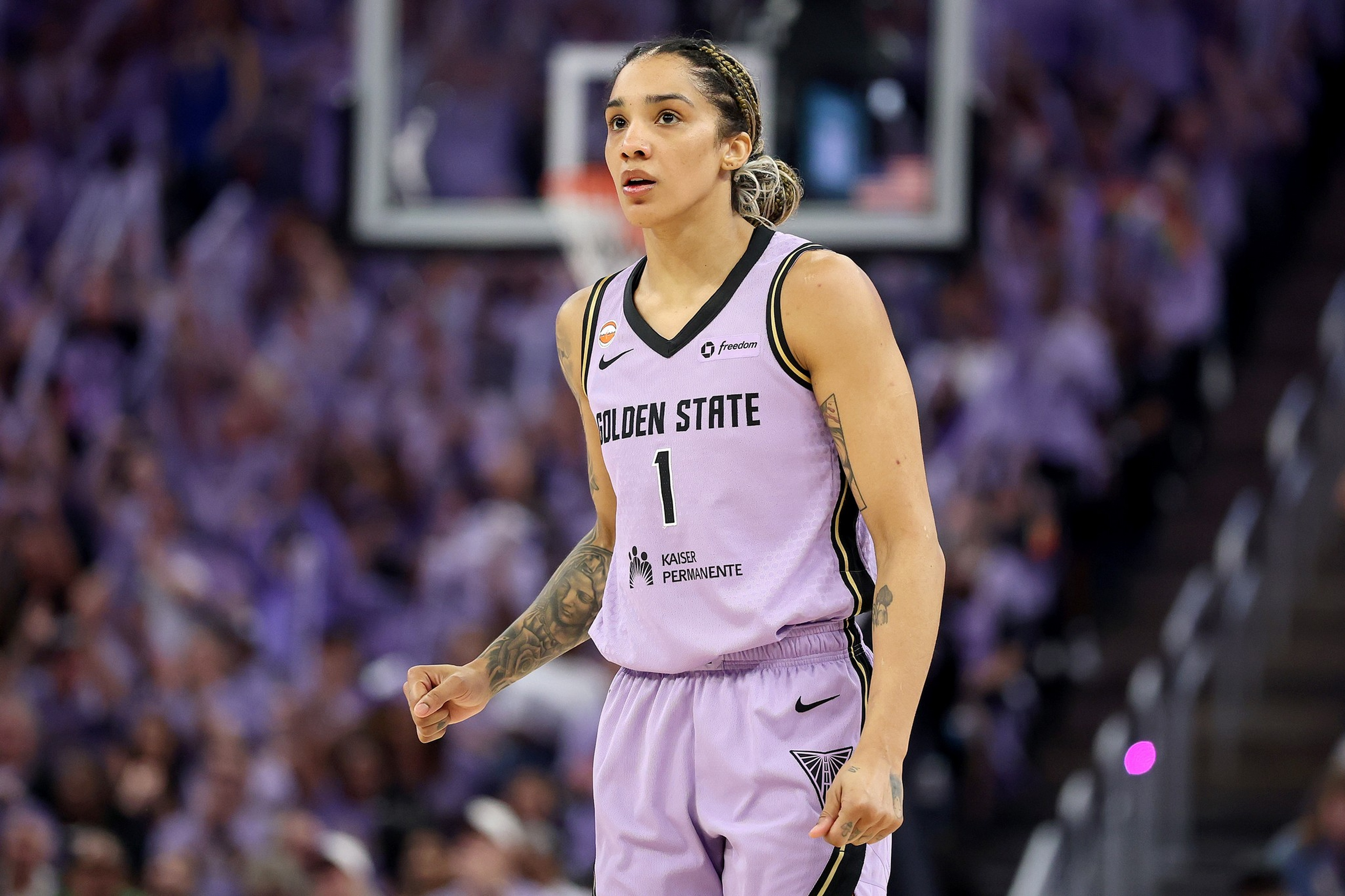 A female basketball player in a lavender Golden State jersey numbered 1 stands on the court with a focused expression and clenched fist.
