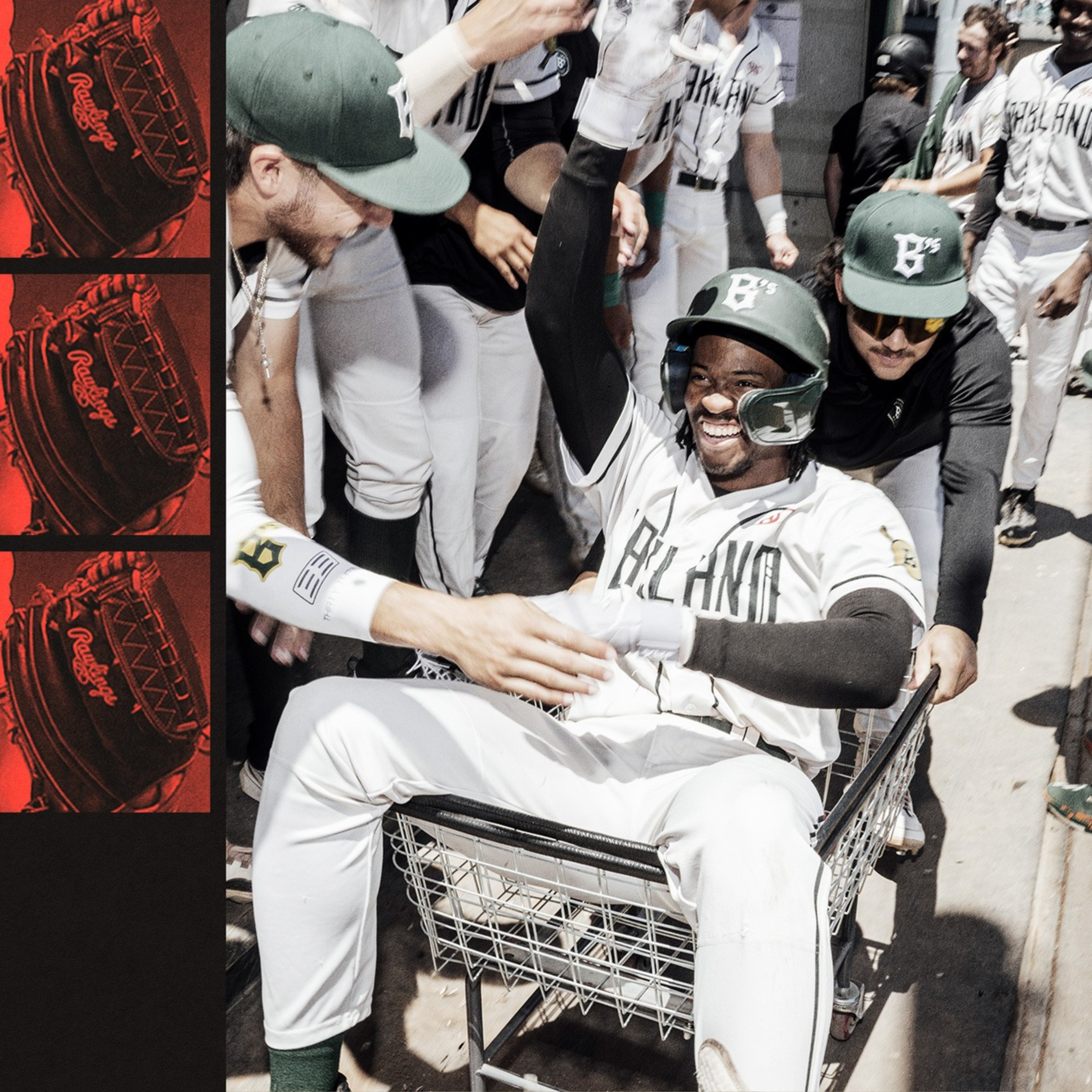 A joyful baseball player in a helmet and uniform sits in a laundry cart while teammates push and cheer around him in a dugout walkway.