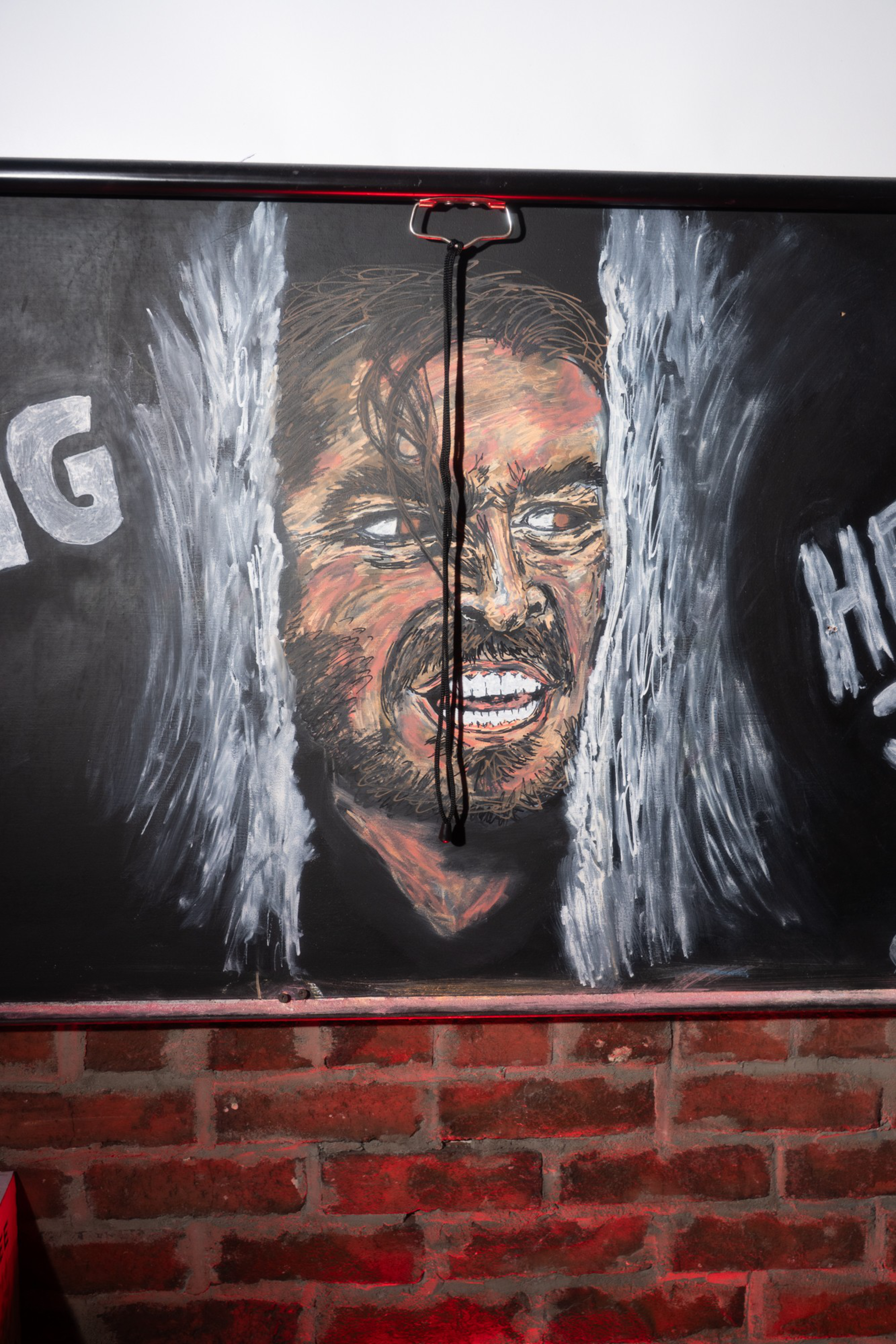 A chalk drawing depicts a man’s intense face peering through parted curtains with clenched teeth, set against a dark background above a brick wall.