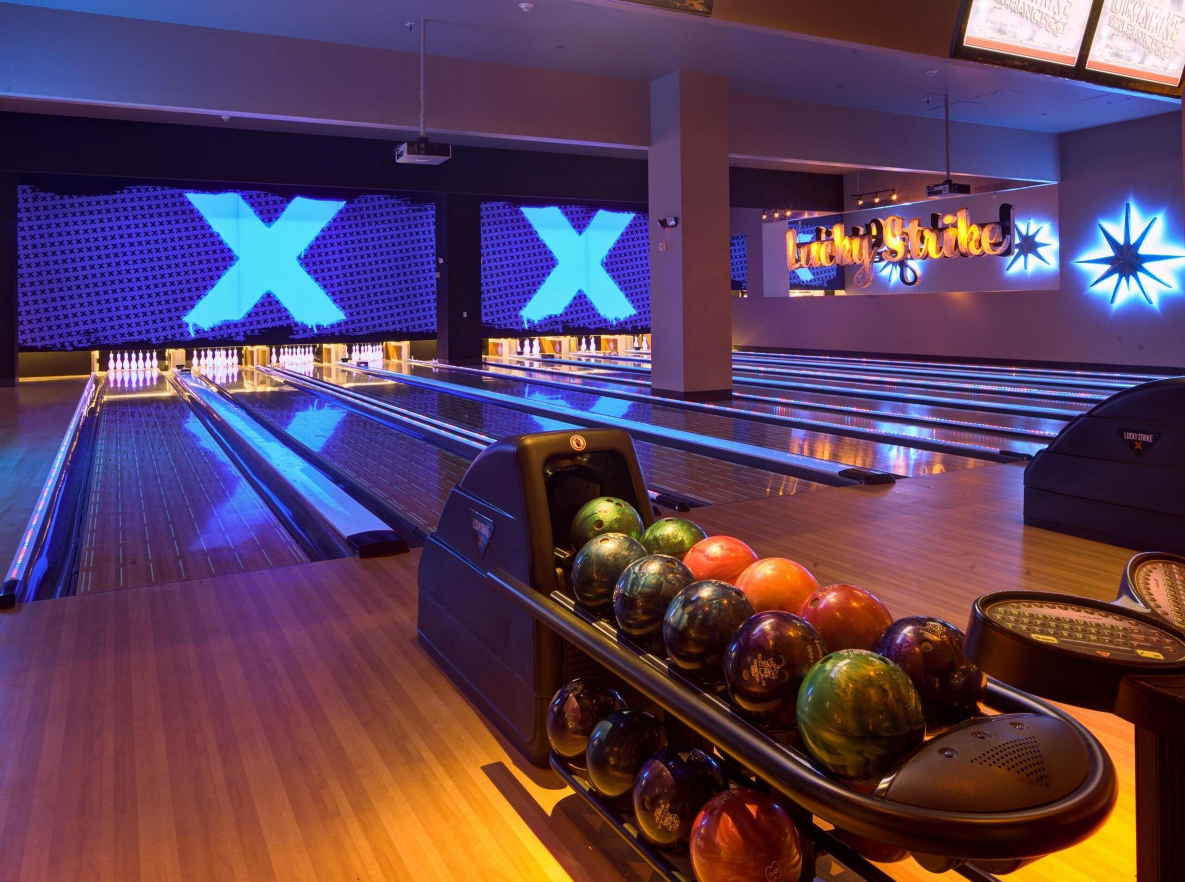 A rack of bowling balls are lined up in a bowling alley.