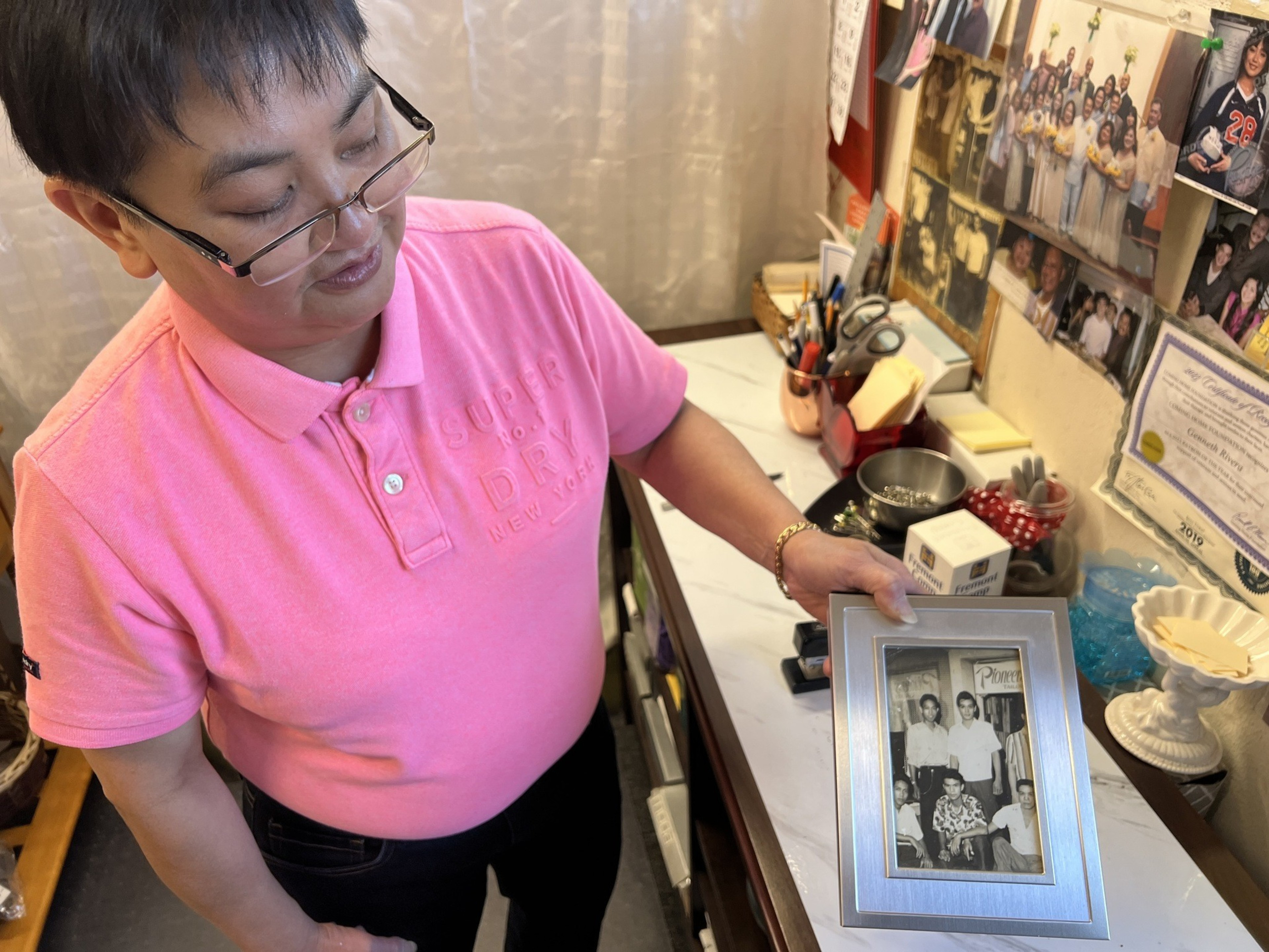 A person in a pink shirt and glasses holds up a black and white photo.