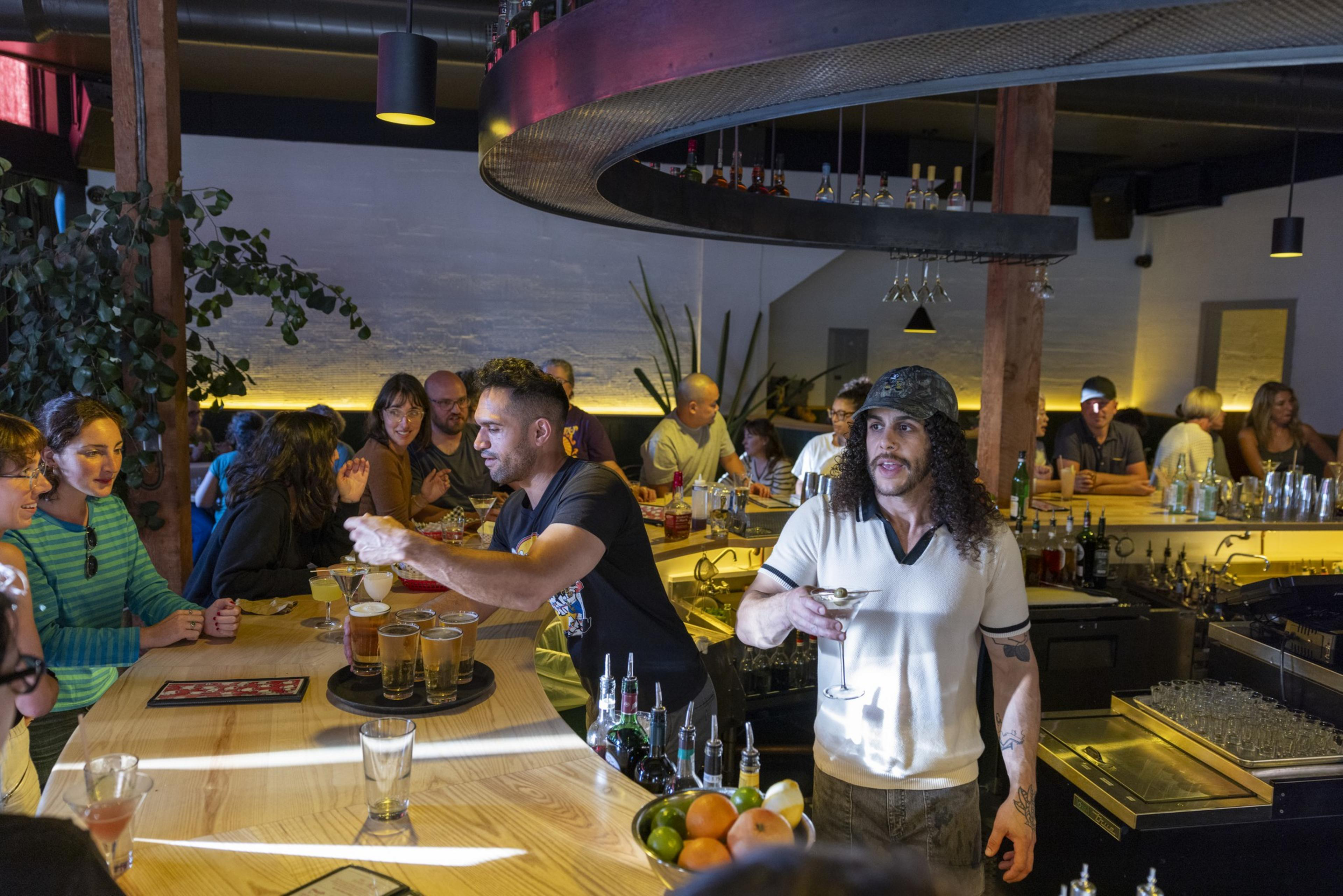 A lively bar scene features patrons conversing and enjoying drinks, while bartenders serve various beverages. The atmosphere is warm with modern industrial décor.