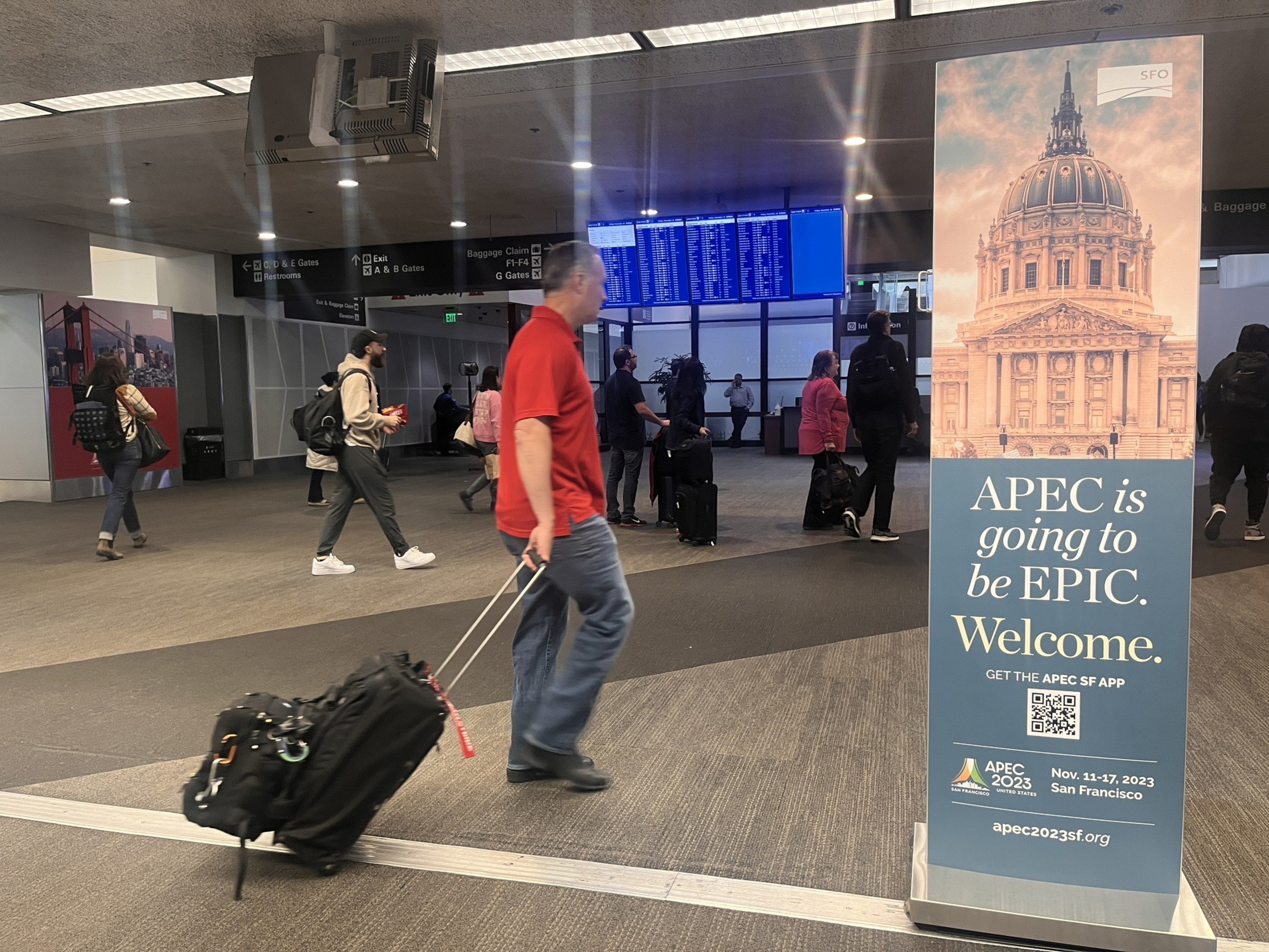 A man with a suitcase passes a sign promoting the APEC summit at San Francisco international airport.