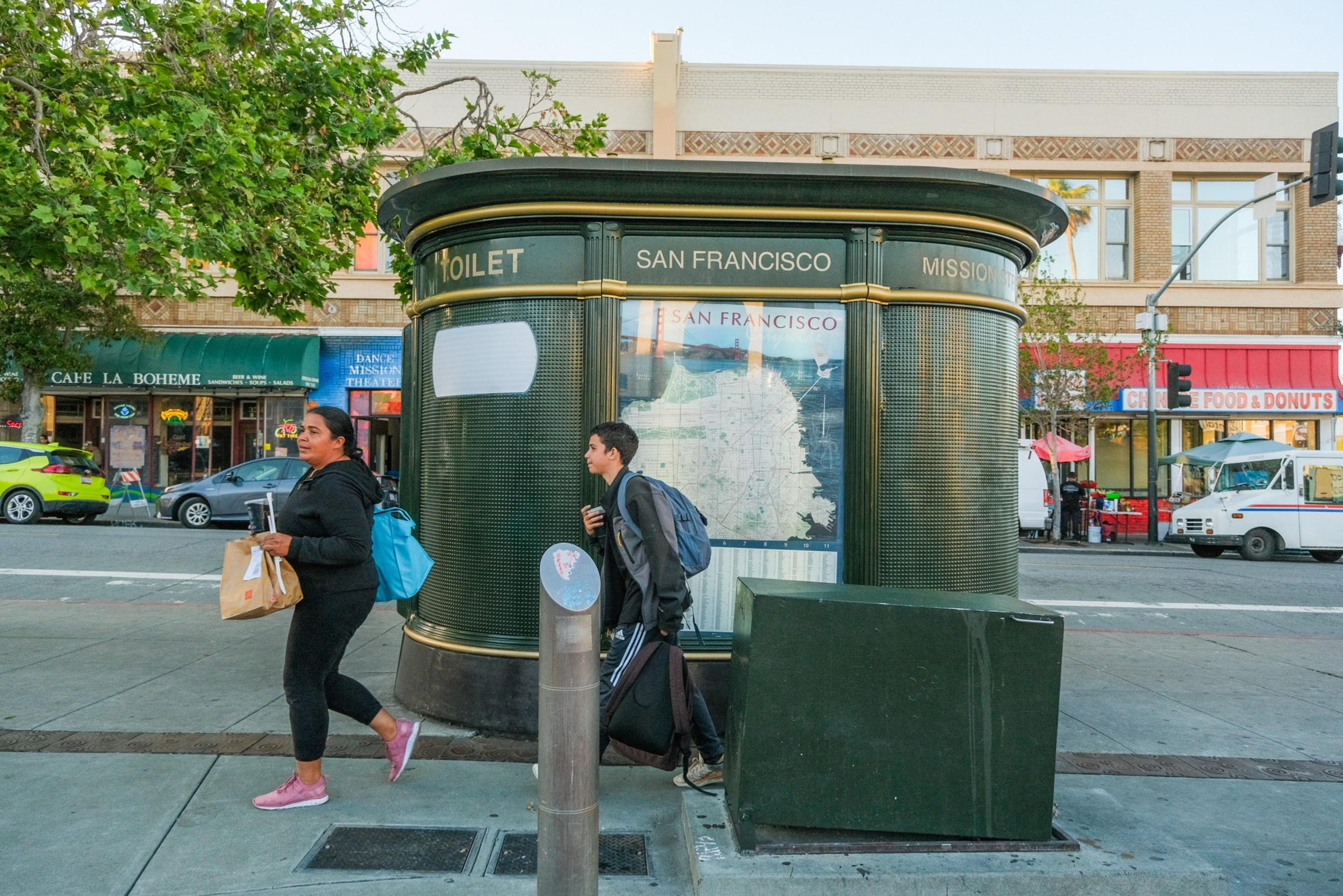 A self-cleaning public toilet in San Francisco with people walking by on the sidewalk.