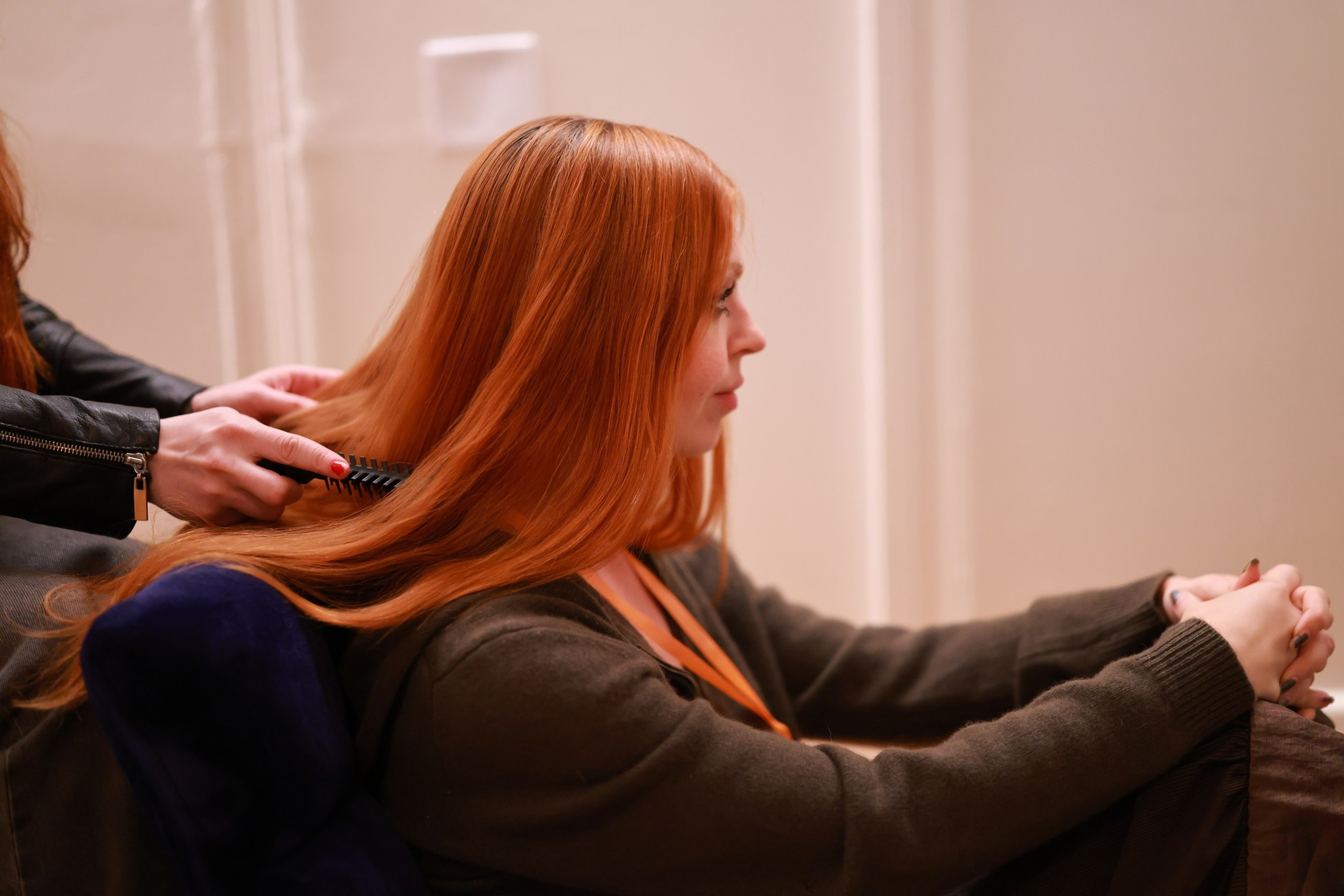 A person with long red hair sits calmly while another person combs their hair, focusing on the smooth strands being brushed.