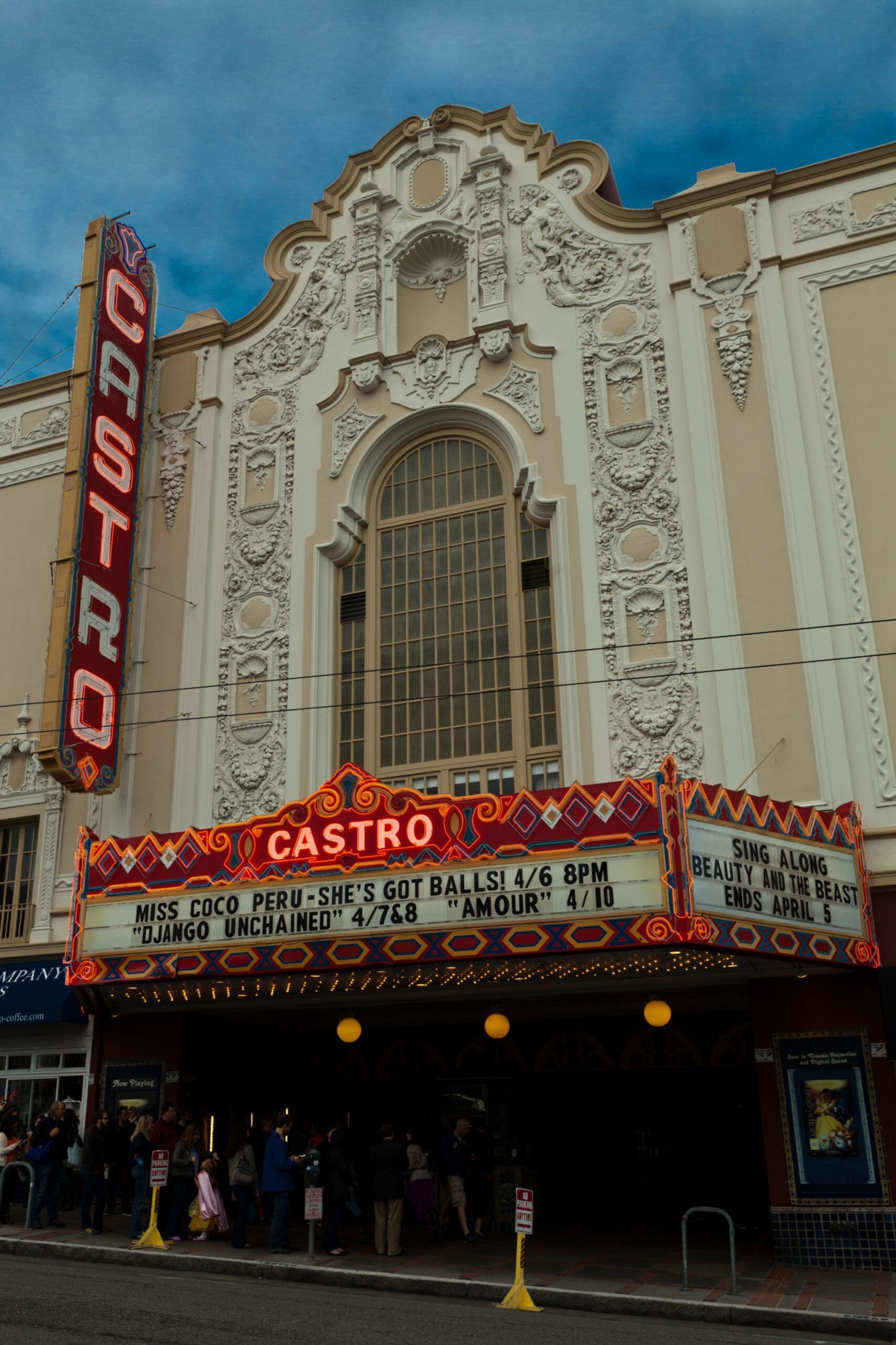 A historic theater with ornate white facade and tall arched window, featuring a vertical red "CASTRO" sign and marquee listing show titles and dates.
