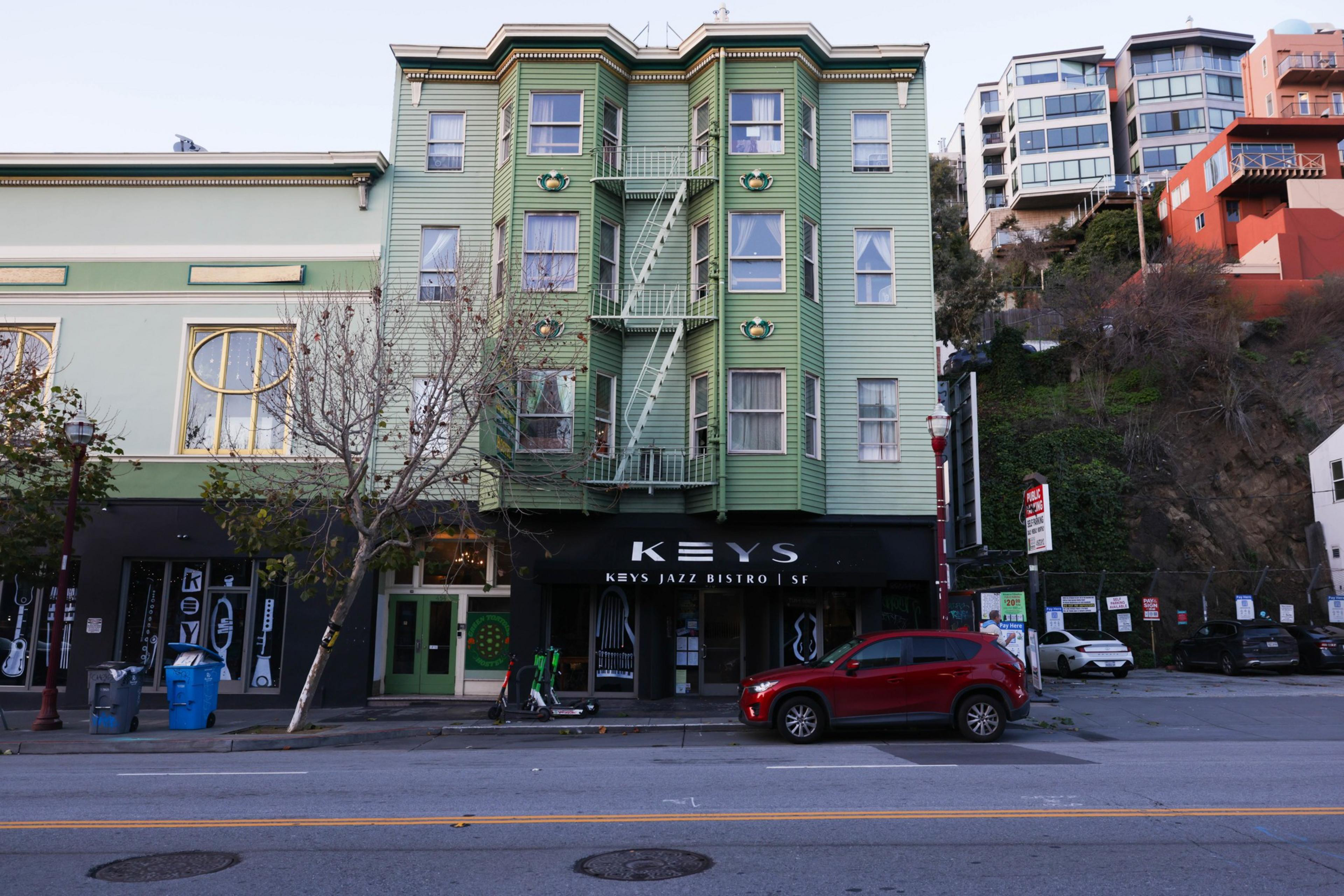 Outside of a hostel that is green with a red car infront. 