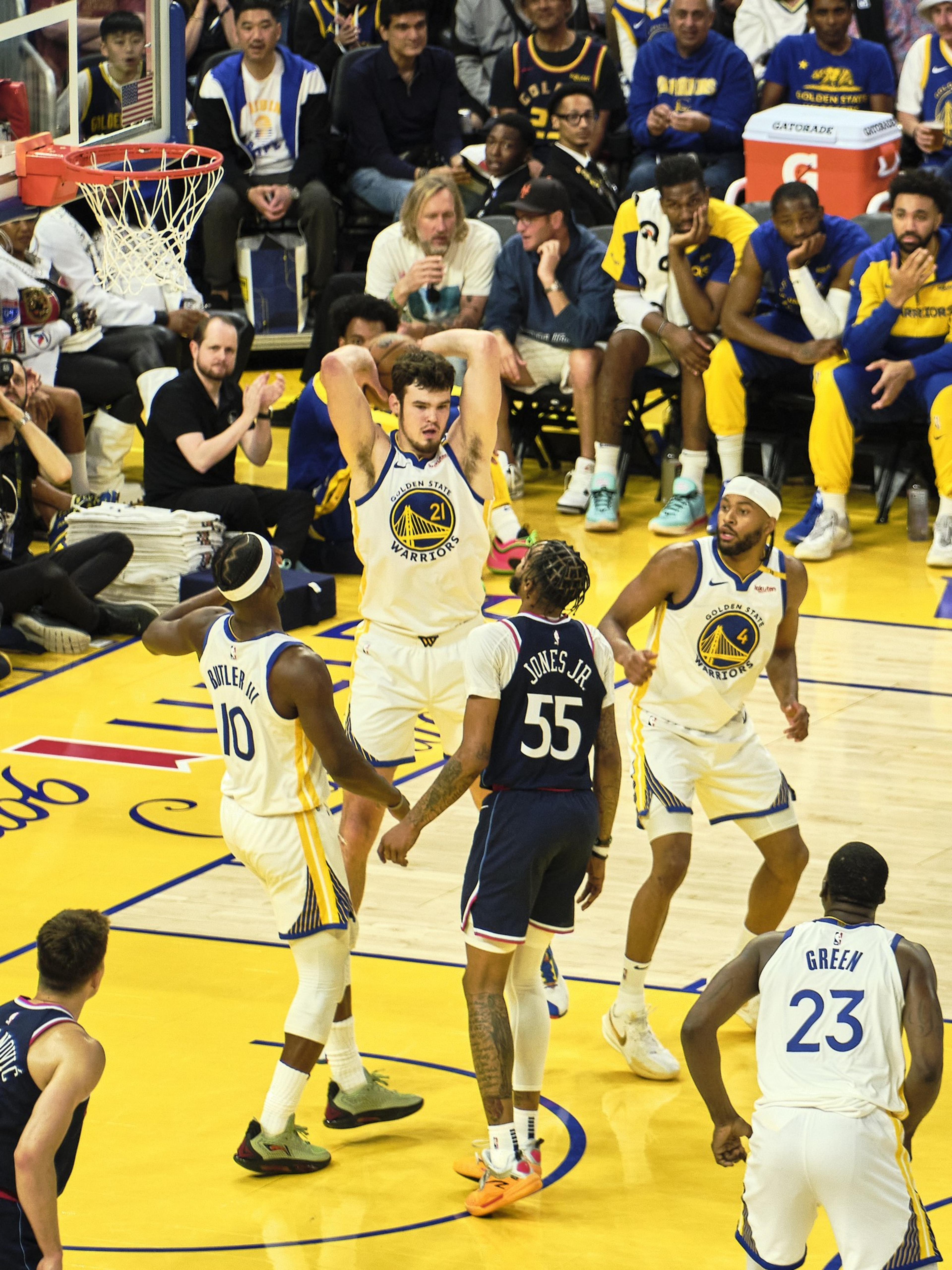 A basketball game is in action with players from the Golden State Warriors and an opposing team maneuvering on the court. The audience watches closely.