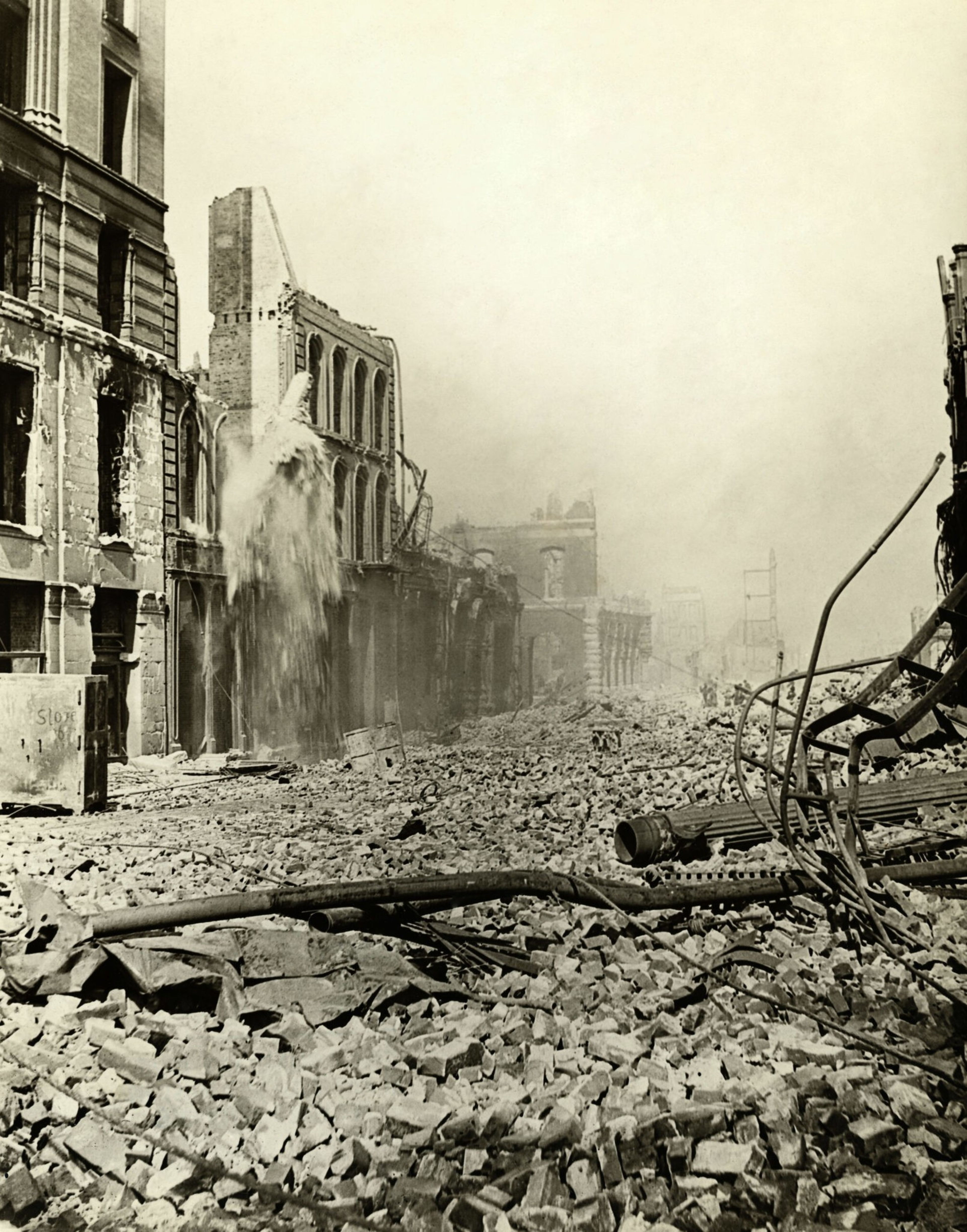 A street filled with rubble and debris from destroyed buildings, with water pouring from a damaged structure, creating a scene of post-destruction ruin.