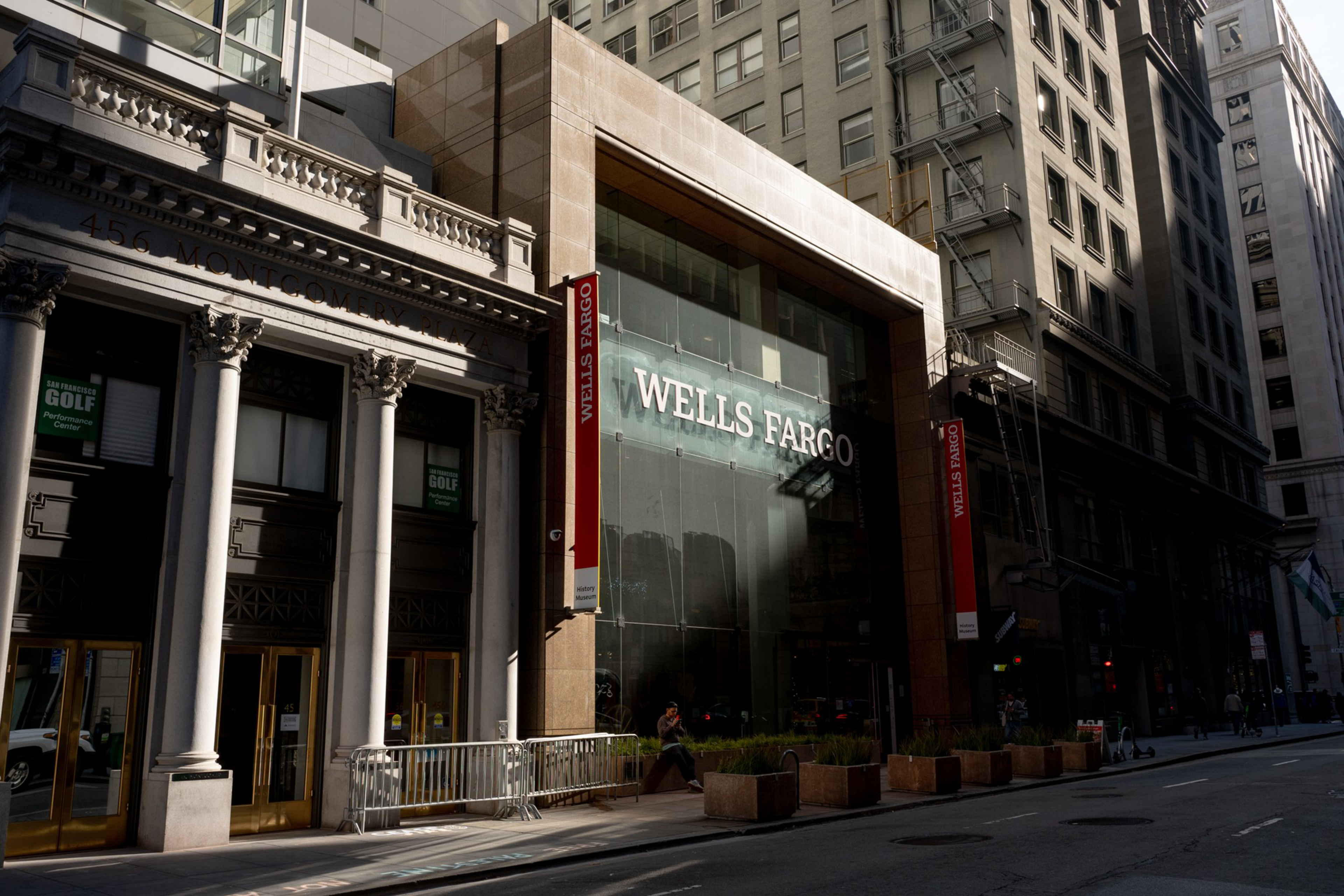 The image shows a city street with a Wells Fargo building featuring a large glass facade. Nearby, a classical building with columns reads &quot;456 Montgomery Plaza.&quot;