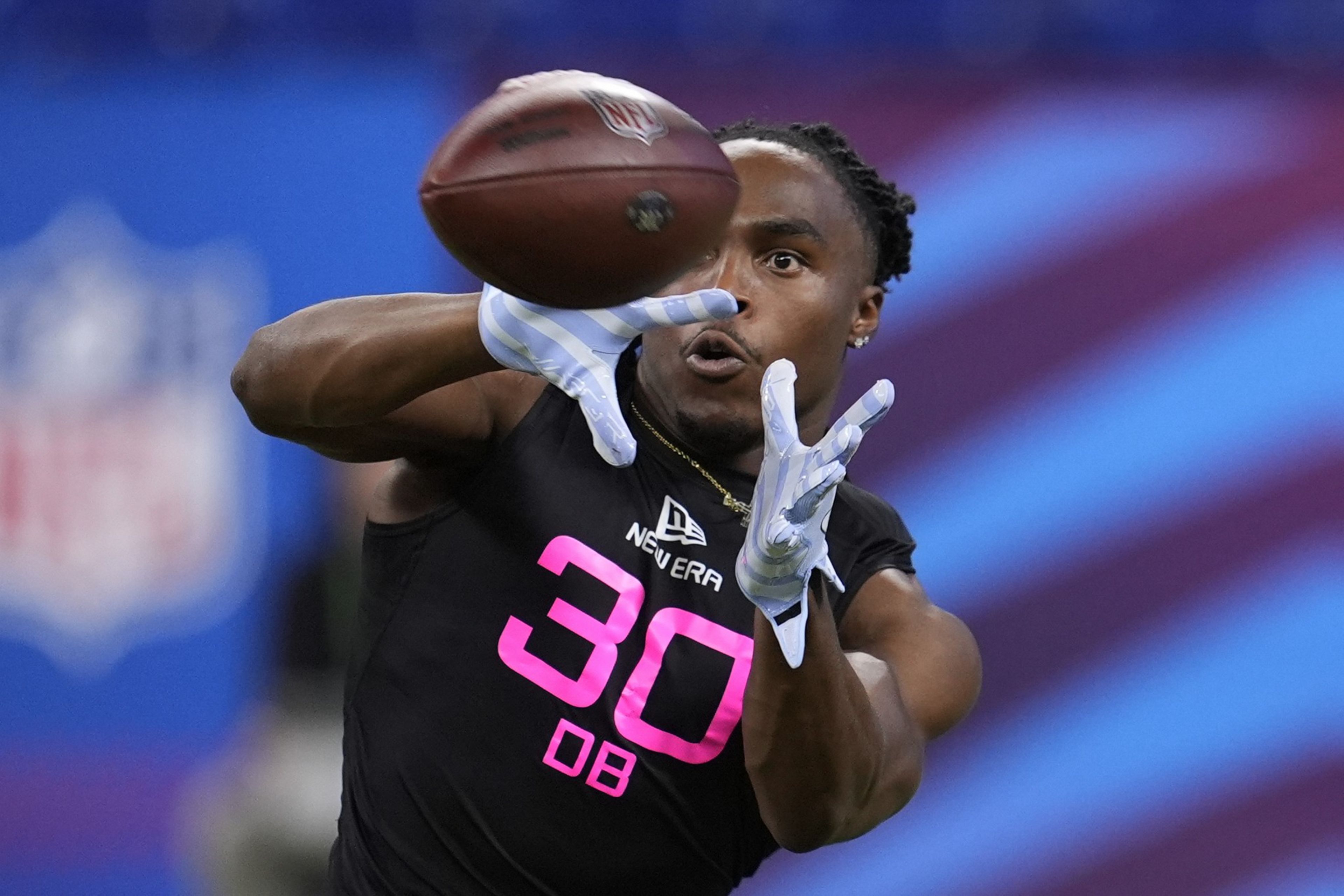 A football player wearing number 30 is reaching out with both hands to catch a football. He is wearing a sleeveless black shirt and white gloves.