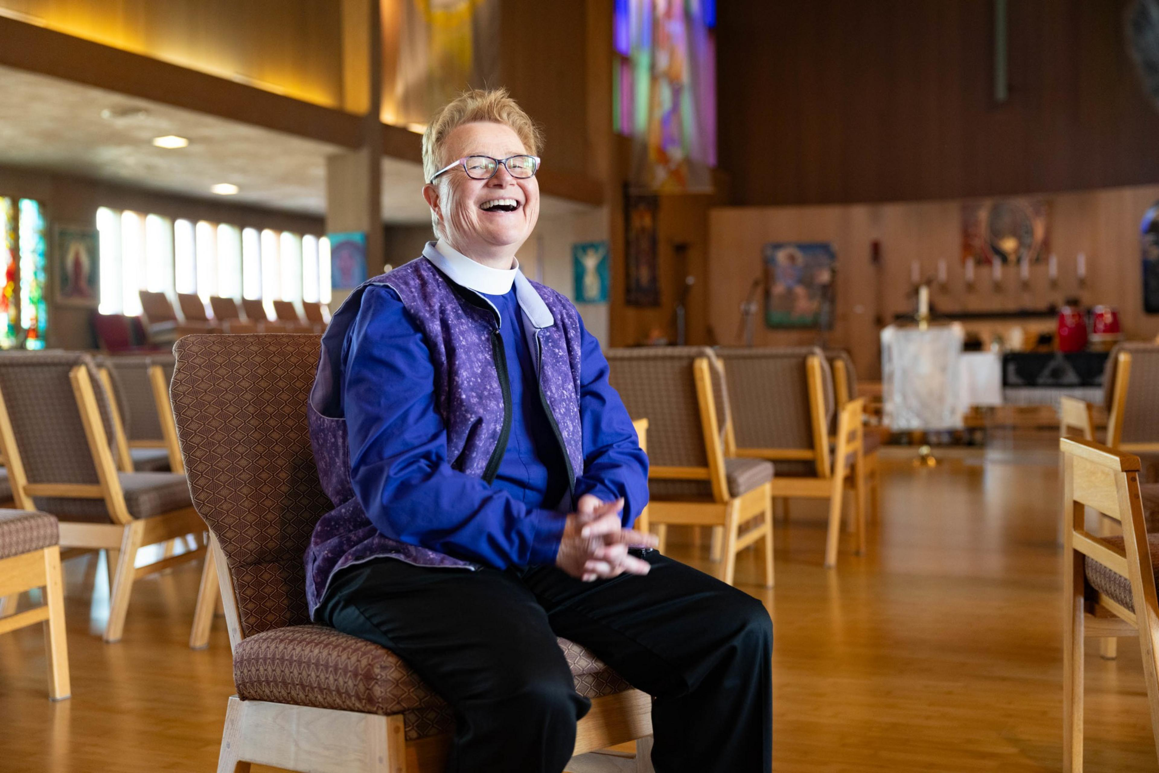 A person sits in a chait in the center of a church smiley widely