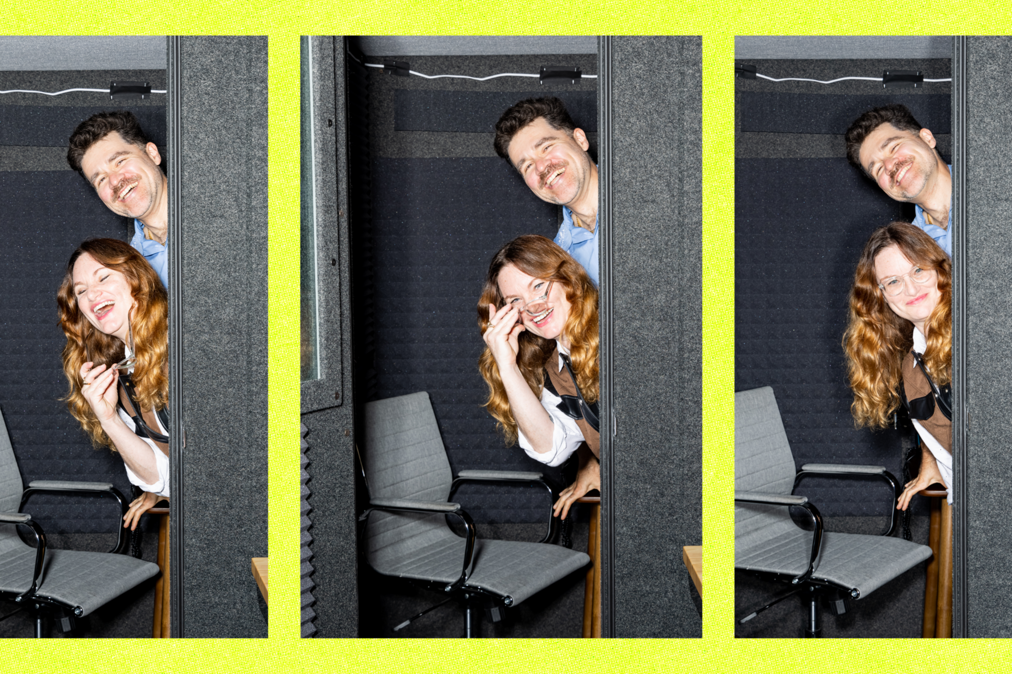 A man and woman with light brown and red hair smile and lean playfully from behind a gray booth wall in a small soundproof room with two gray chairs.