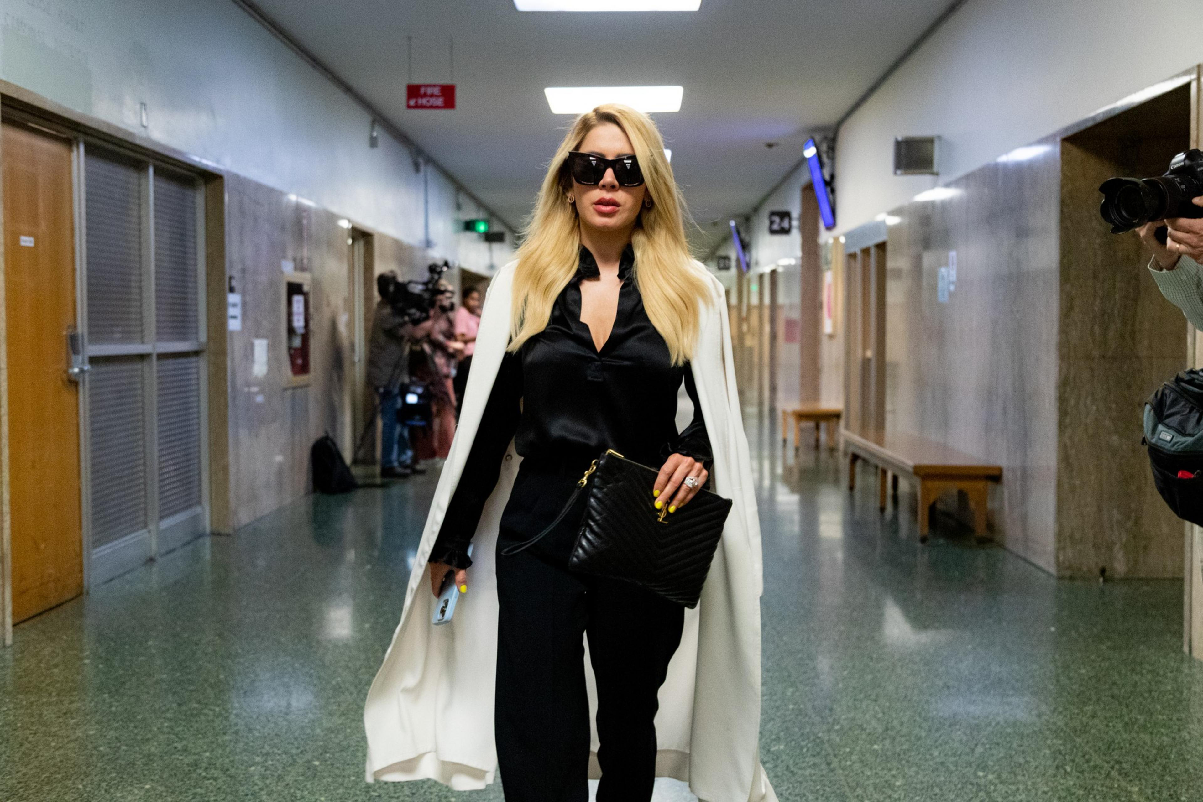 a woman in a white cape and sunglasses walks down a corridor